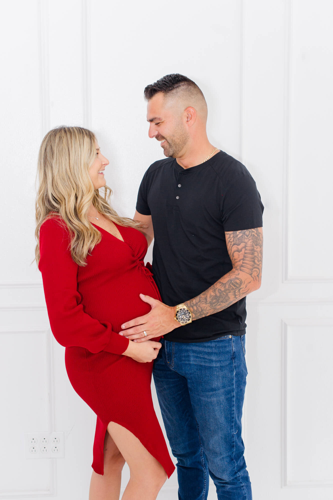 Expectant parents pose smiling at each other in the studio