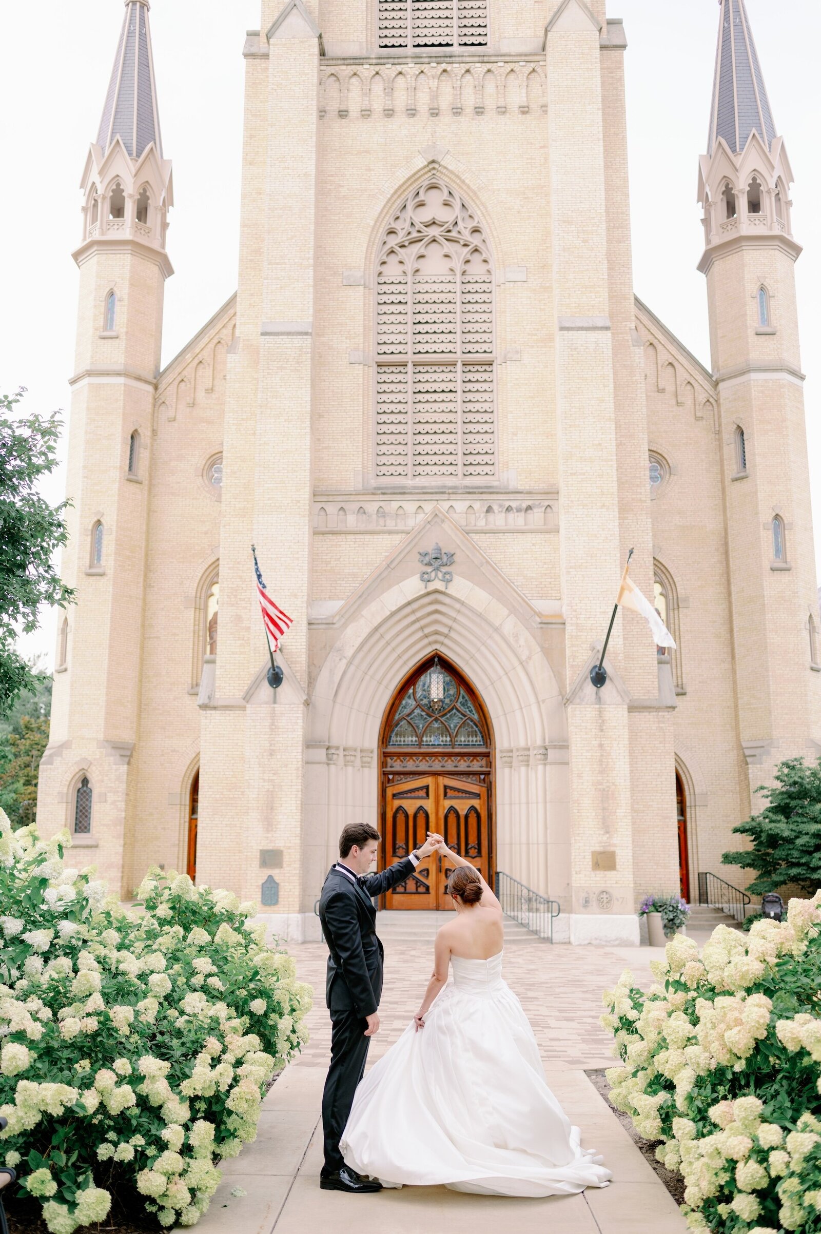 groom twirling bride in front of a Catholic church