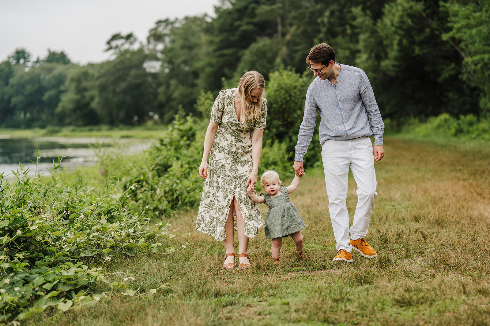 parents hold hands with one year old baby and walk outdoors