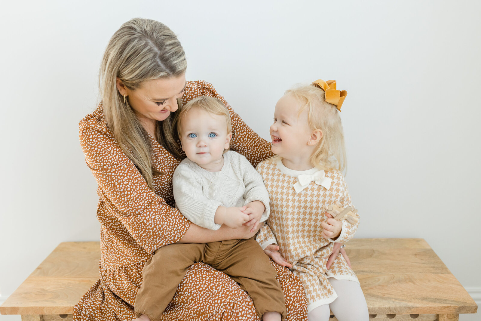 Mother embracing toddler daughter and son in simple white studio