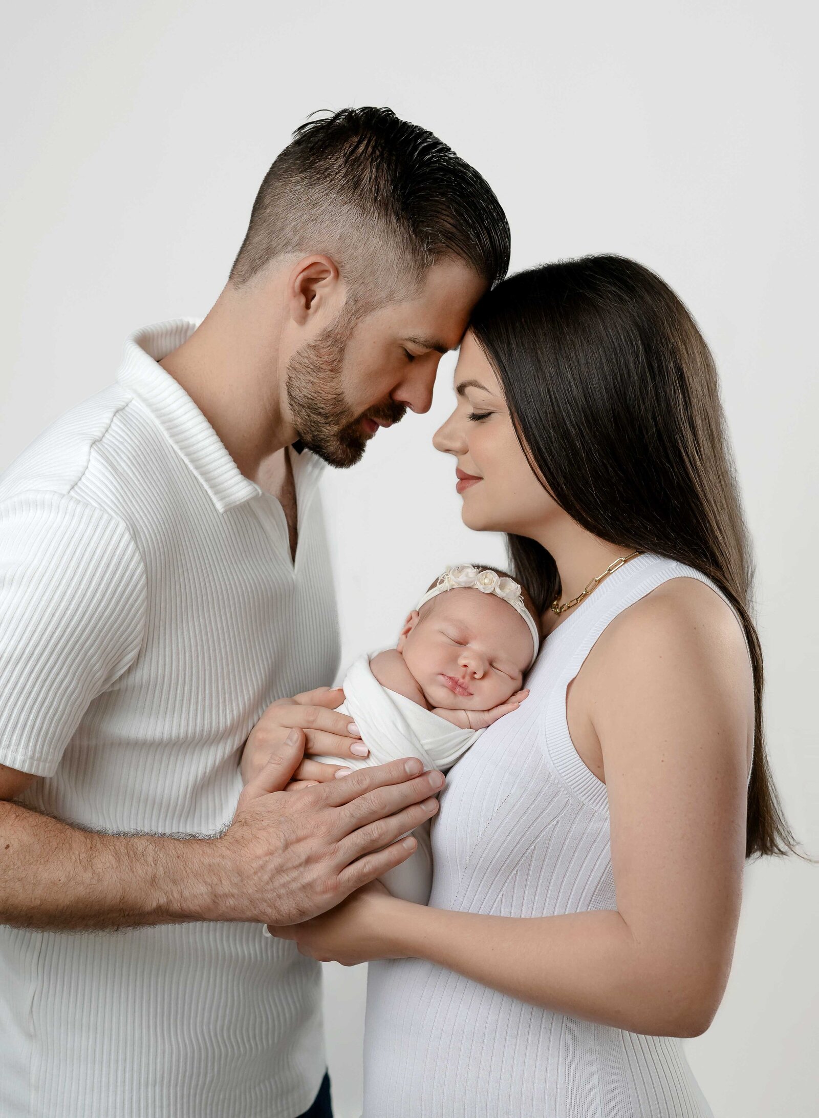 Mom, Dad and baby girl all in white. Baby is snuggled on mom's chest and parents heads together. Photographed at Woodstock studio, close to Atlanta.