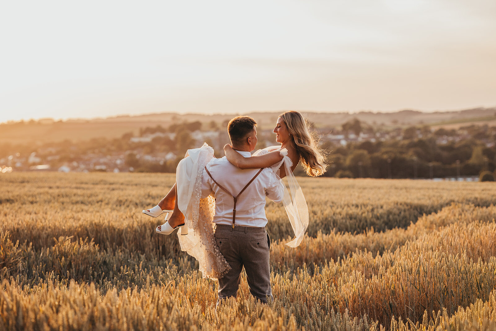 groom carries bride in corn field