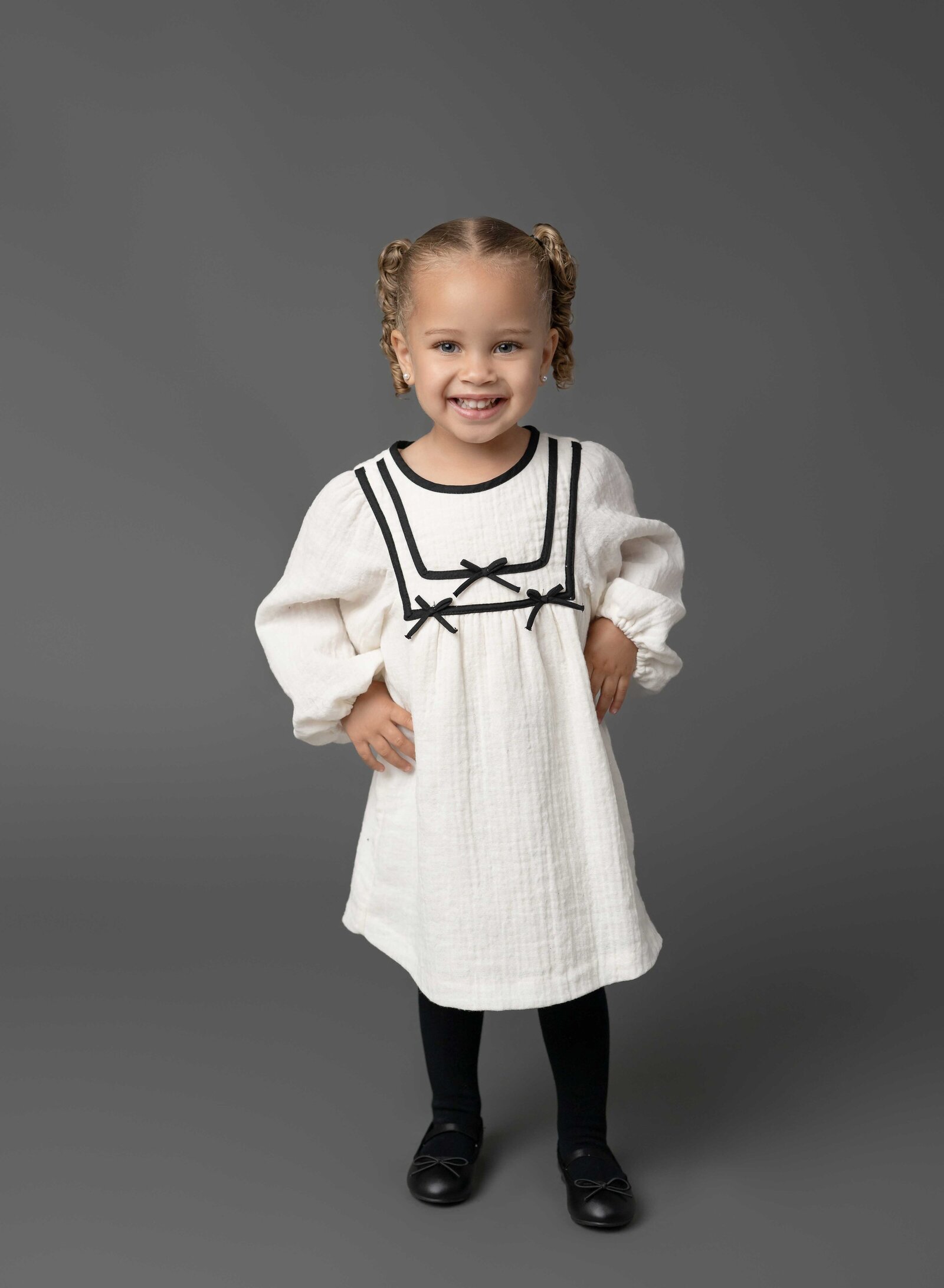 Girl in white dress with hands on hip, smiling. Family photo taken at Atlanta Photo Studio by Jenni Nikki Photography.