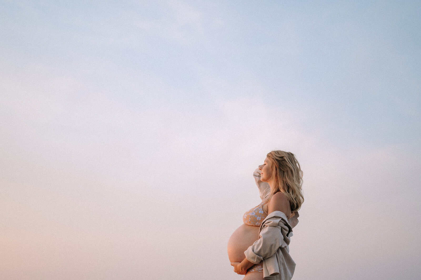 pregnant woman stands on beach at sunset during maternity photoshoot