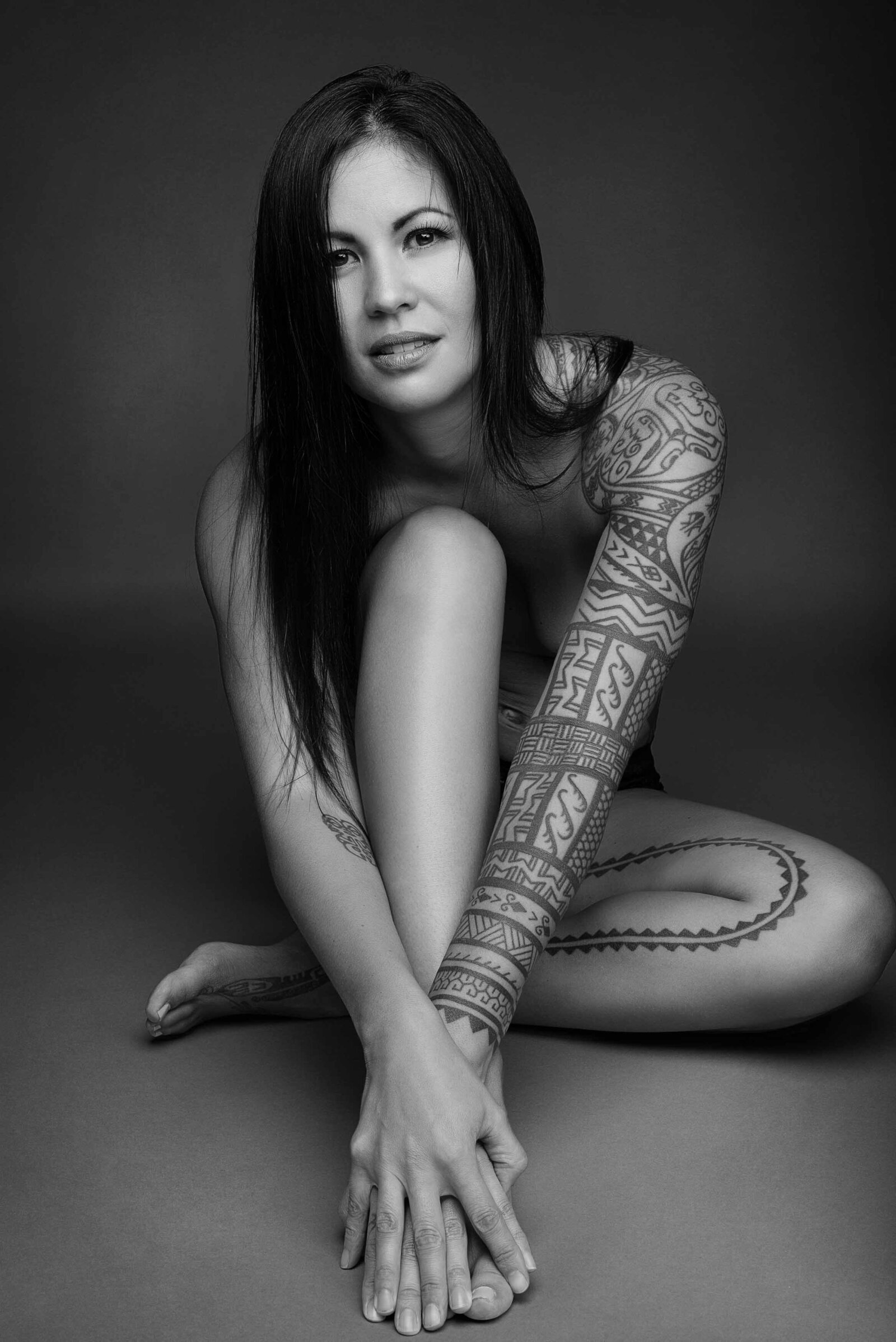 nude woman with tattoos sitting on floor