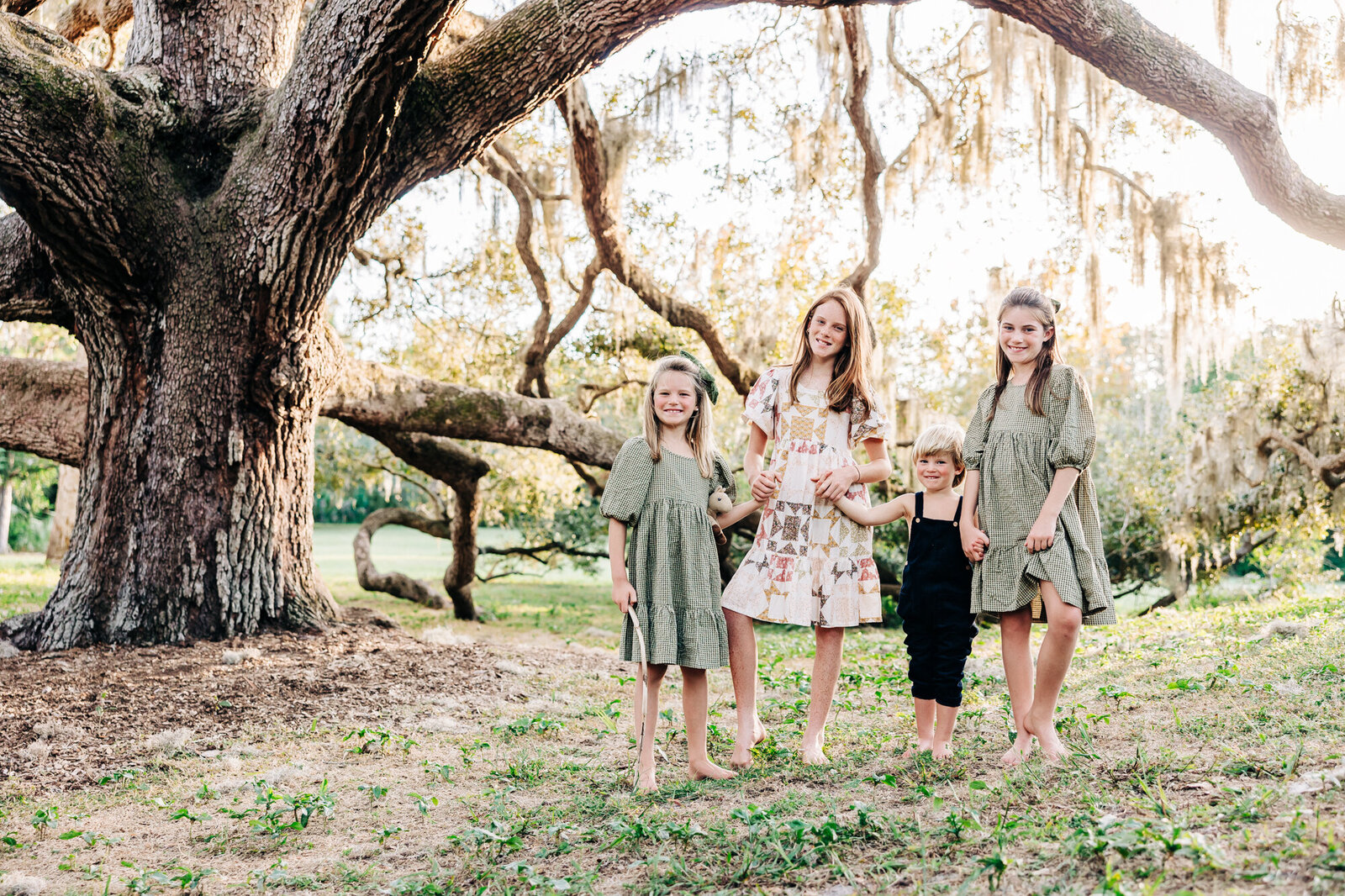 Emotive photos of 4 siblings holding hands in a park near st. pete with a large oak tree