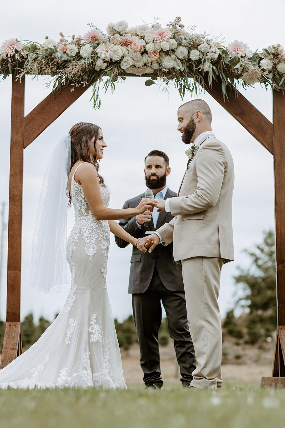 A couple exchanging vows under a floral arch in an outdoor ceremony