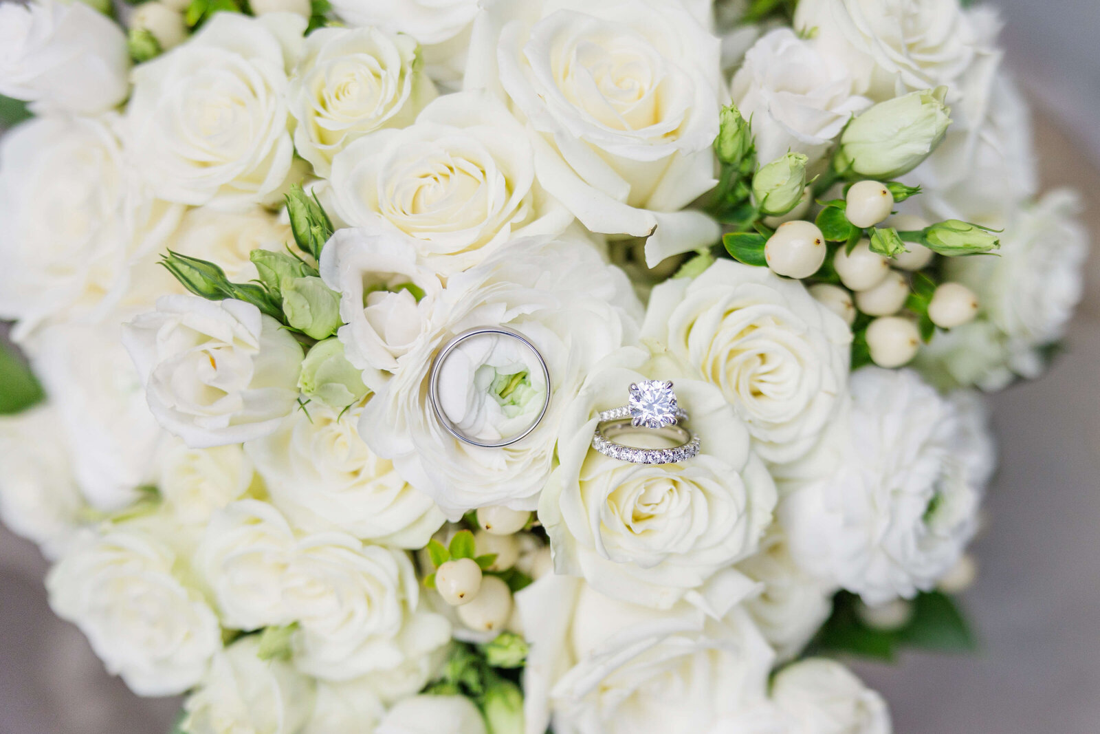Close up photo of a white wedding bouquet with a man and woman's wedding rings.