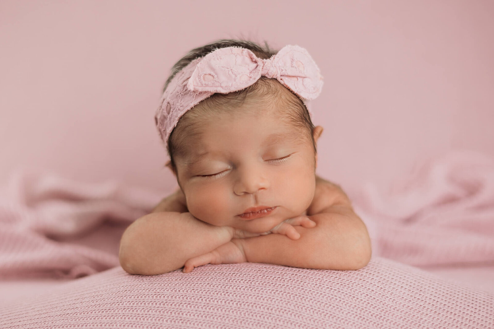 Baby girl with her head resting on her hands posed in studio with a pink headband on during her newborn session