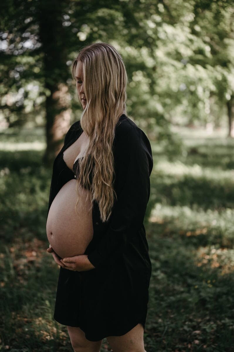 Kvinna håller om sin gravida mage i grölnskan.