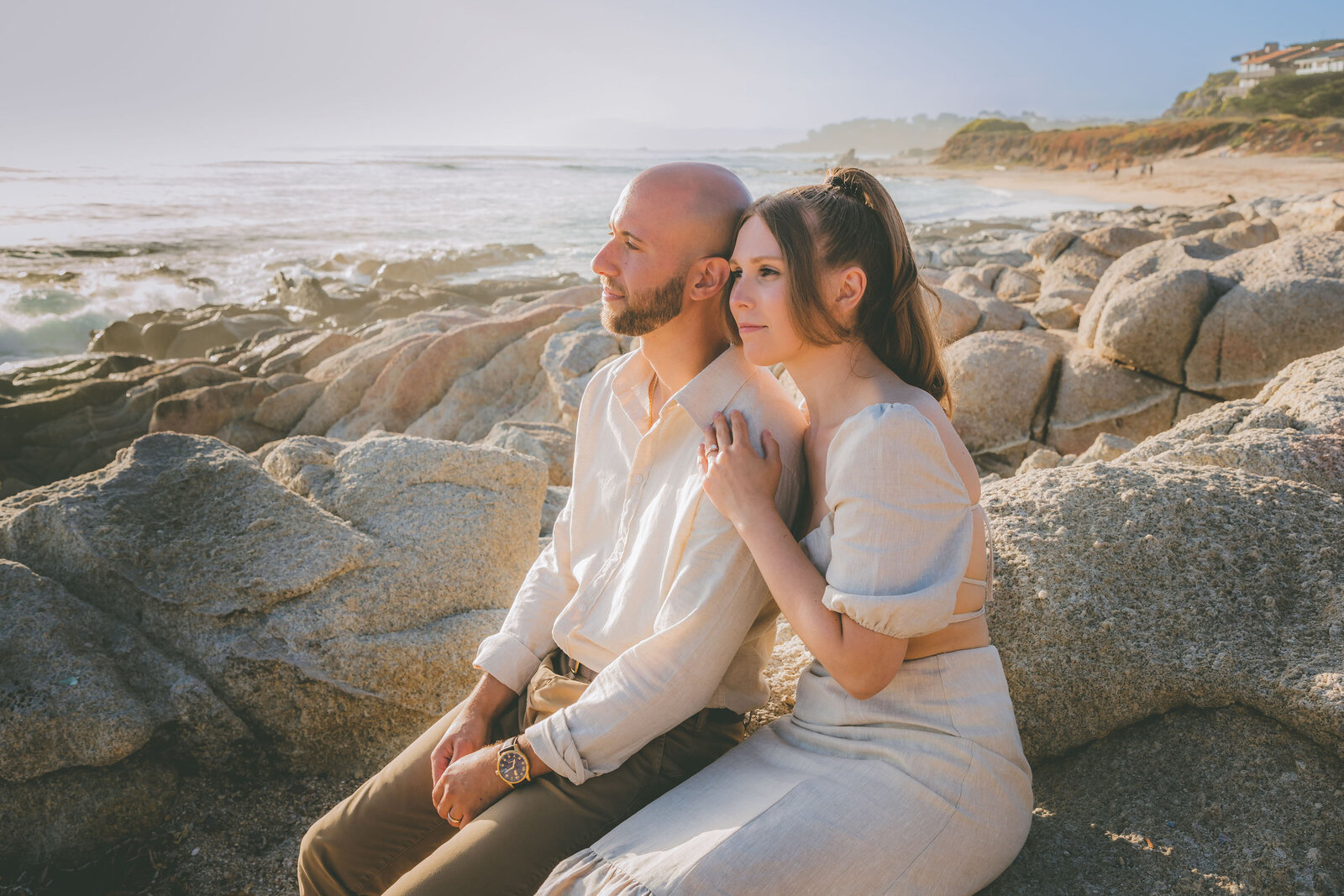 A couple sits on large rocks at the beach and look out into the ocean during their elopement.