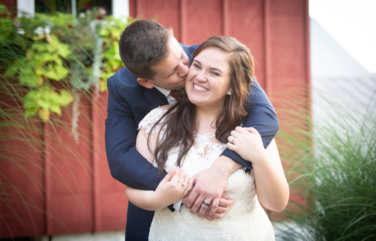 groom kisses bride's cheek in front of red building