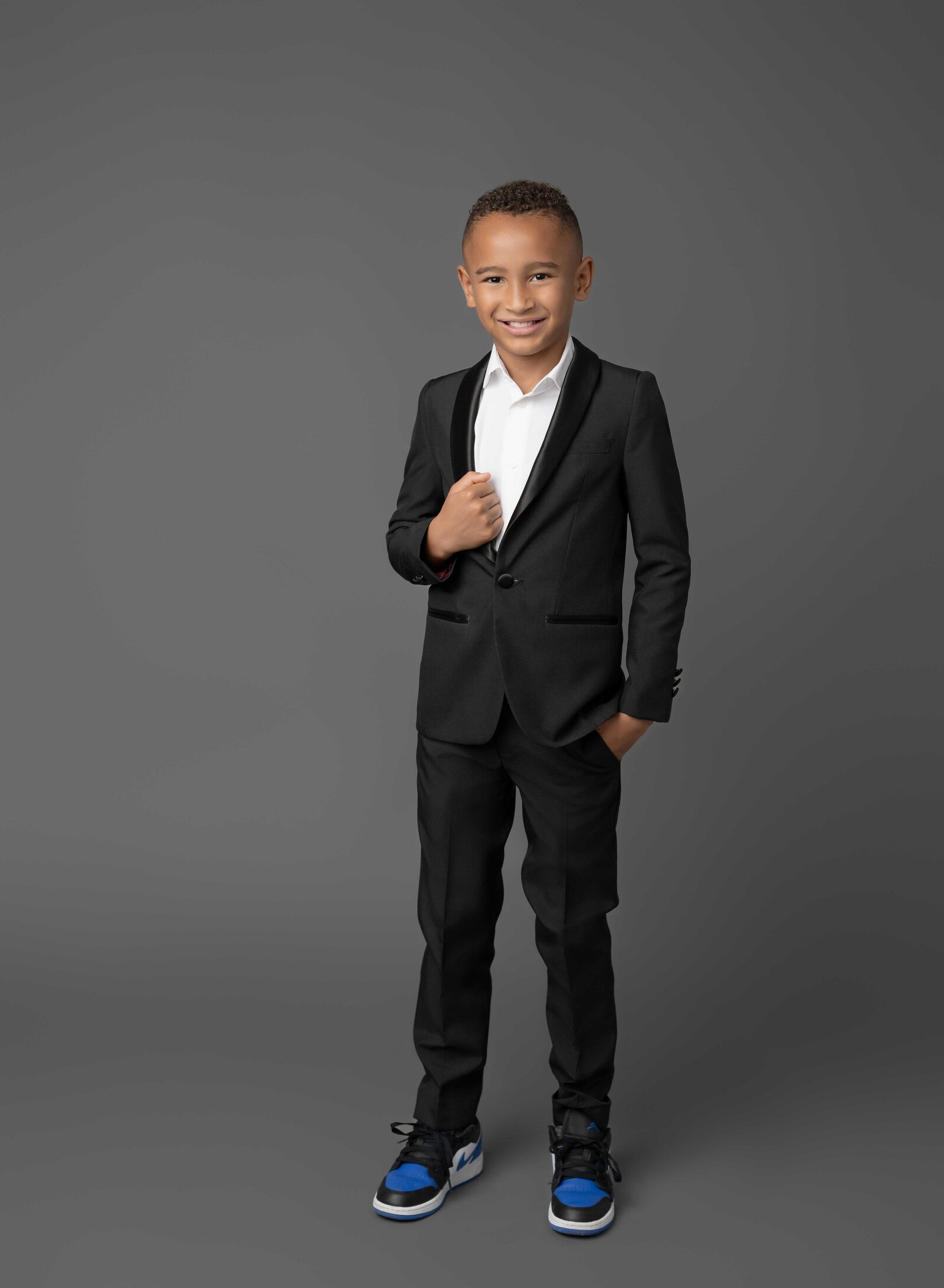 Boy dressed in black suit and smiling at camera. Family photo taken at Atlanta Photo Studio by Jenni Nikki Photography.