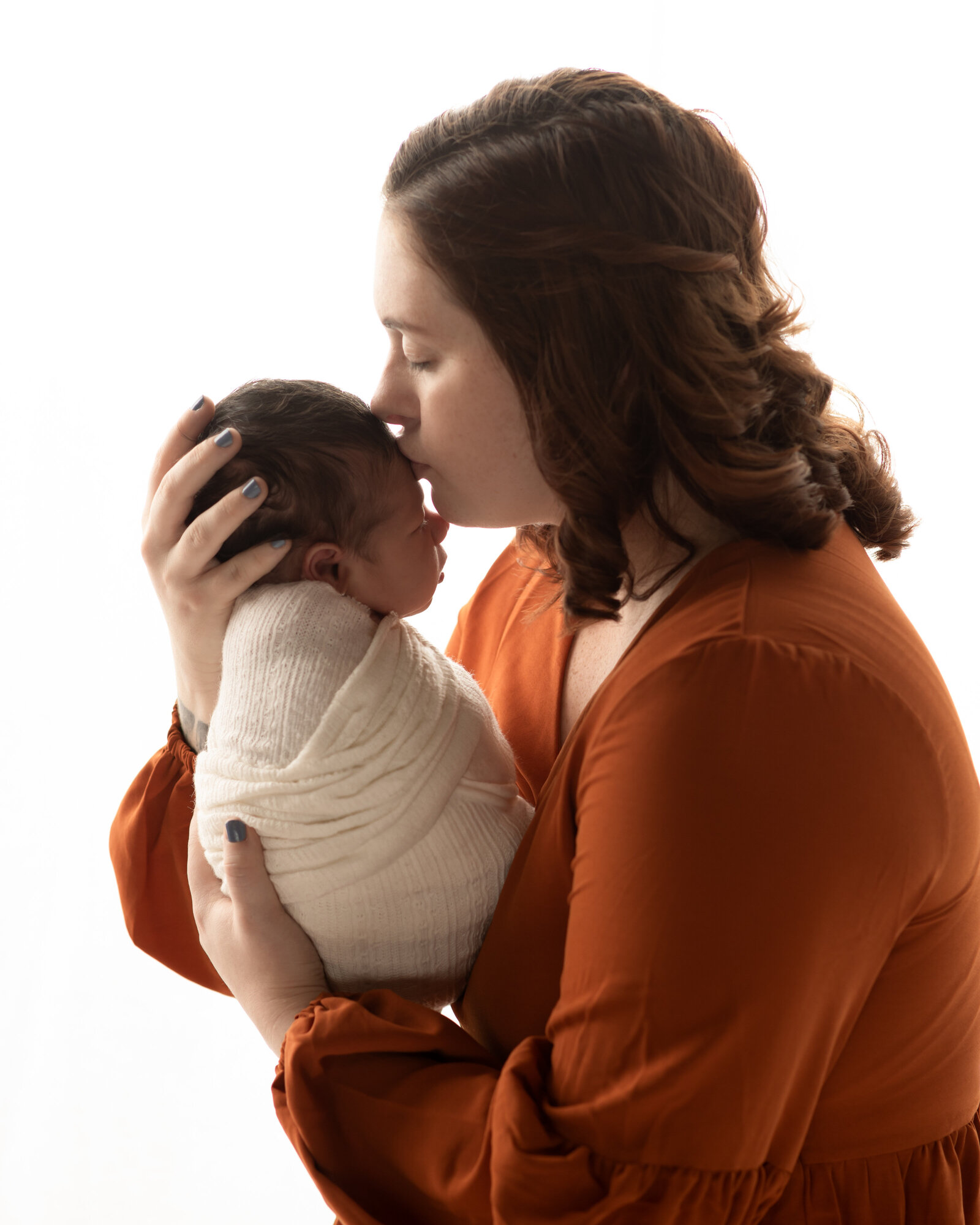 mom kissing newborn son on forehead for studio photoshoot cleveland newborn photographer