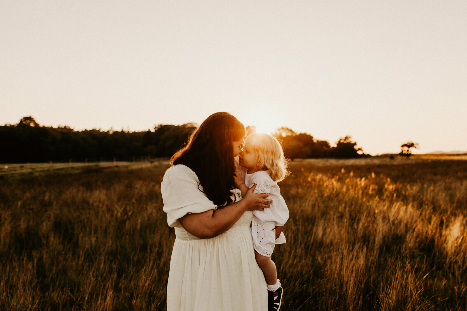 en mamma och henns dotter pussar varandra med solen strålar mellan sig på ett vackert guldigt fält
