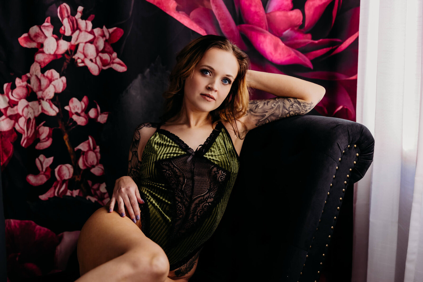 stunning woman with blue eyes in green velvet lingerie resting her elbow on the back of a chaise during her wisconsin boudoir photography experience