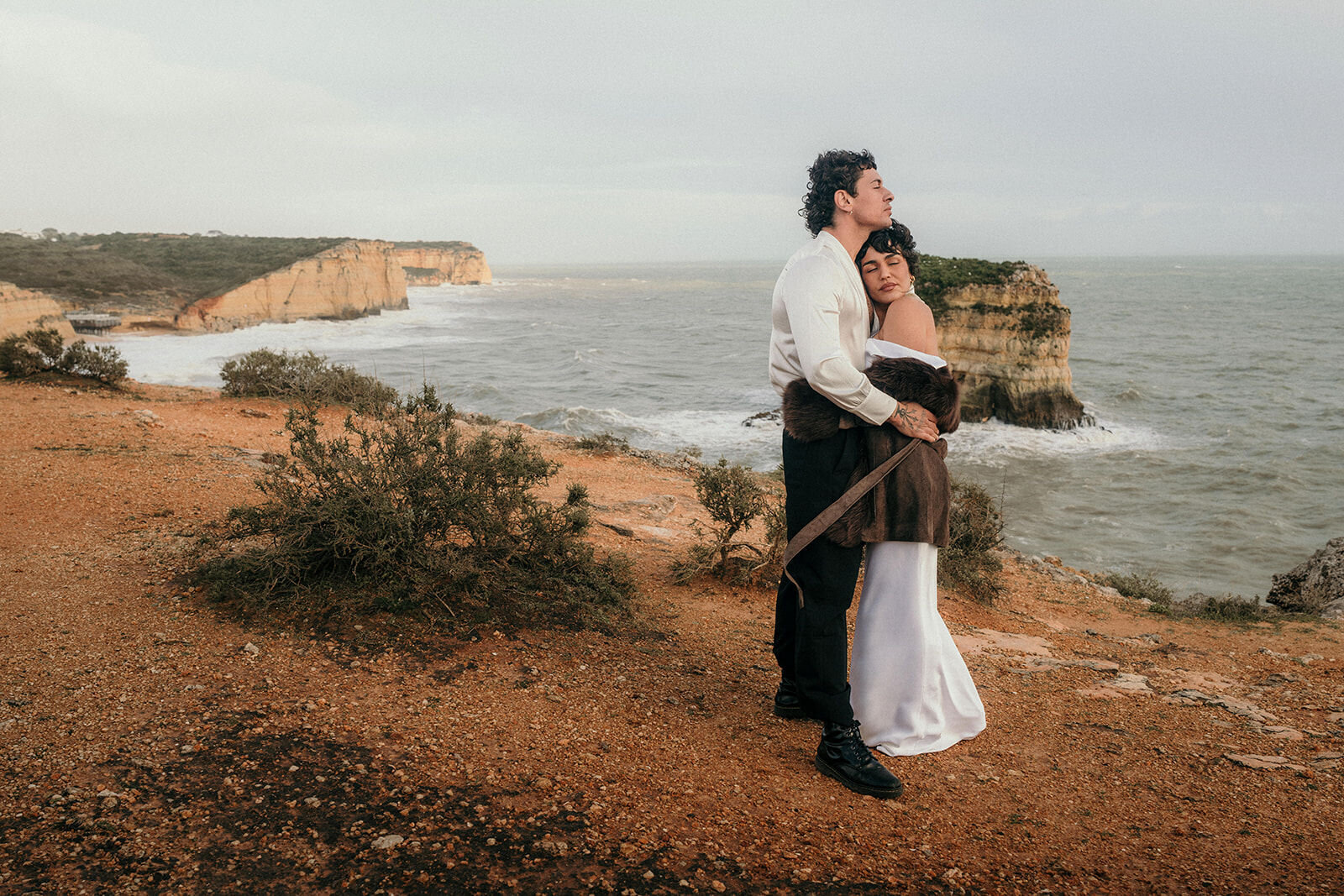 Wedding couple in a close embrace standing on the edge of a cliff with ocean-view.