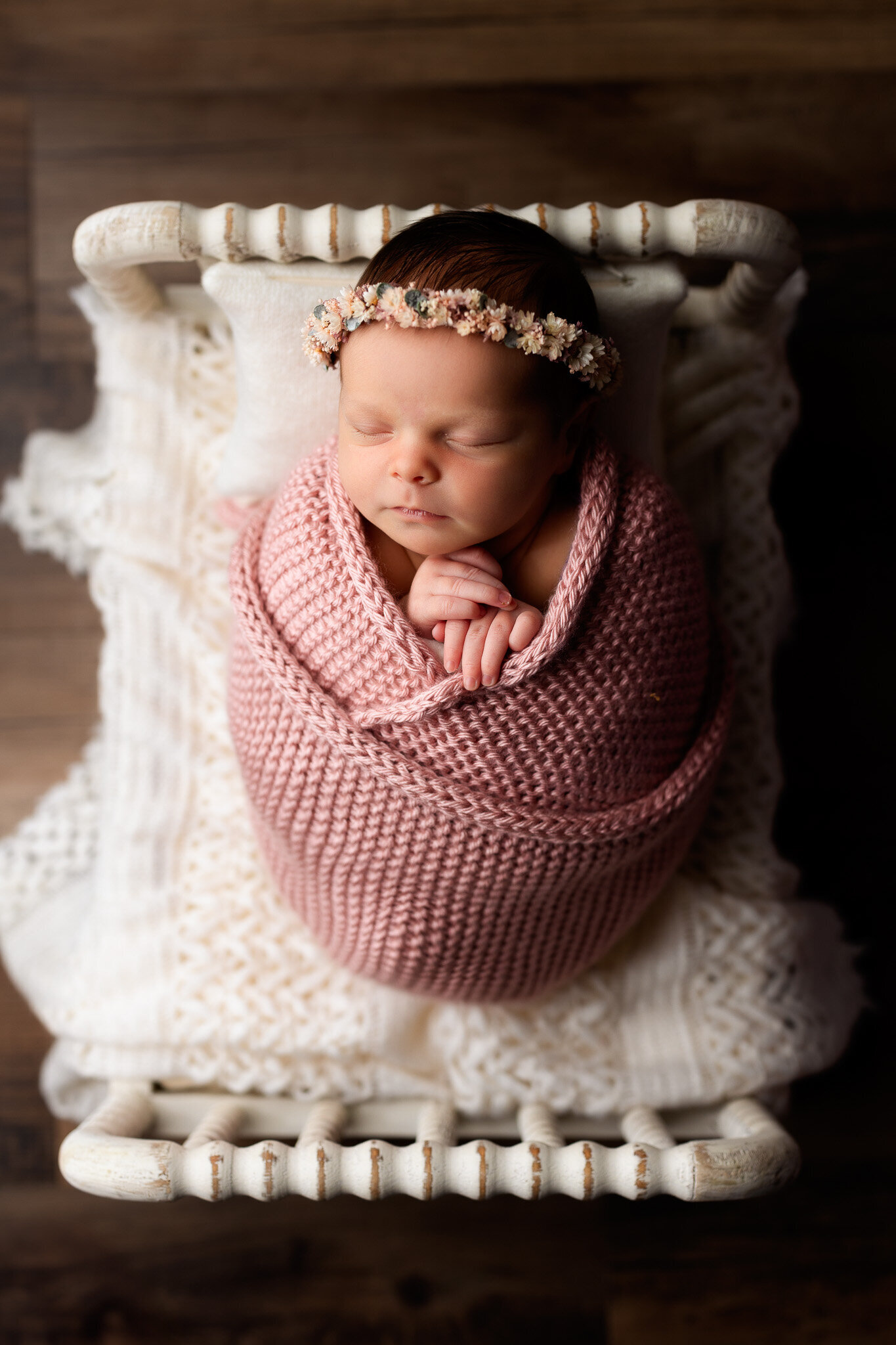 Newborn baby girl swaddled in a pink knit wrap with a floral head band