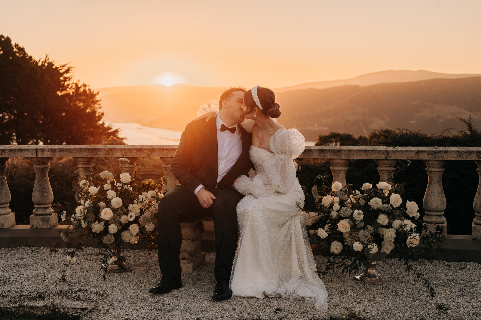 a bride and groom with sunset behind them overlooking dunedin harbour at camp estate larnach castle
