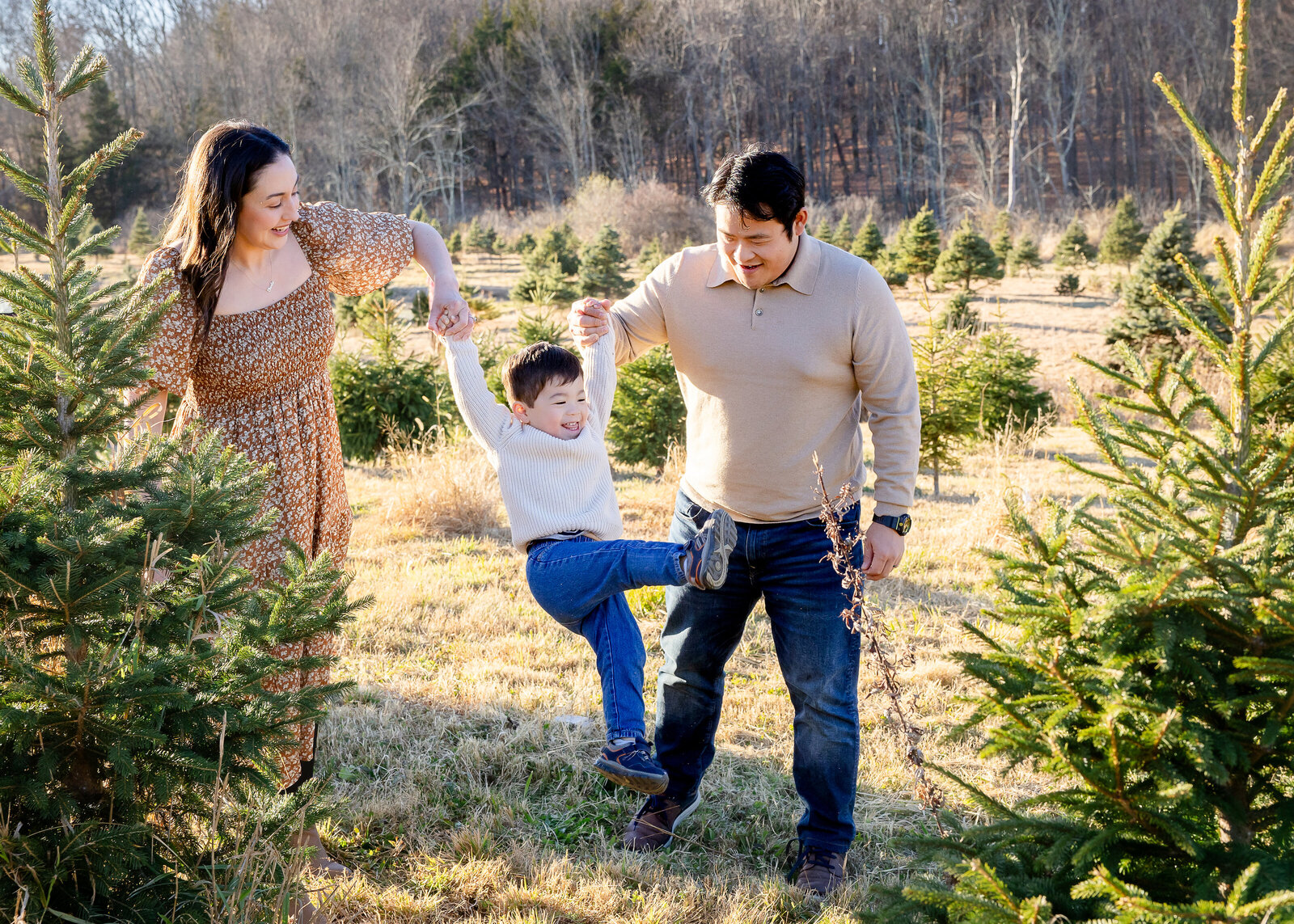 Holiday photo of smiling boy swinging on parents' arms at a Sussex County, New Jersey Christmas tree farm.
