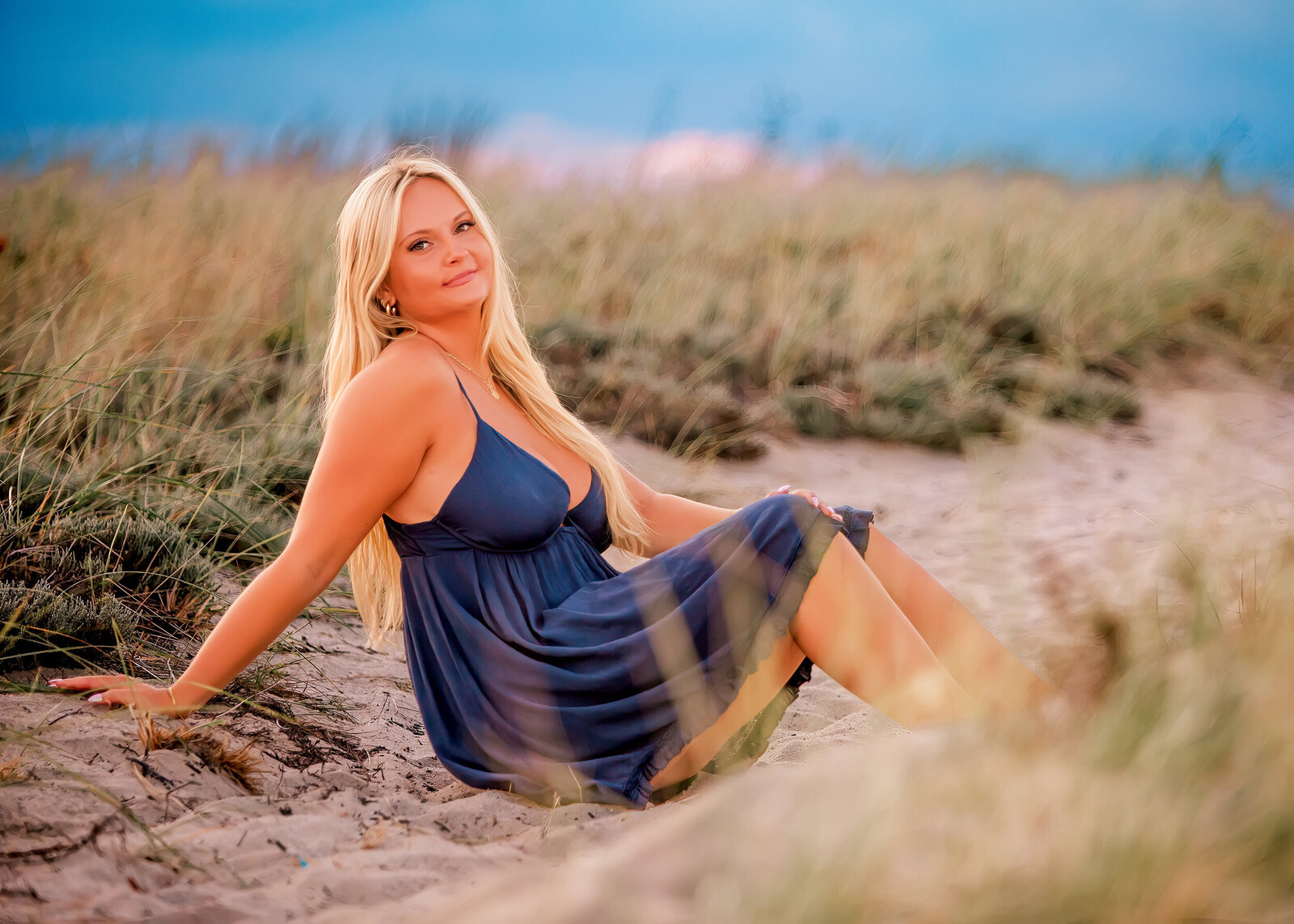  High school senior girl standing on a rock over looking the ocean wearing a blue dress posing for a Cape Cod Portrait Photographer