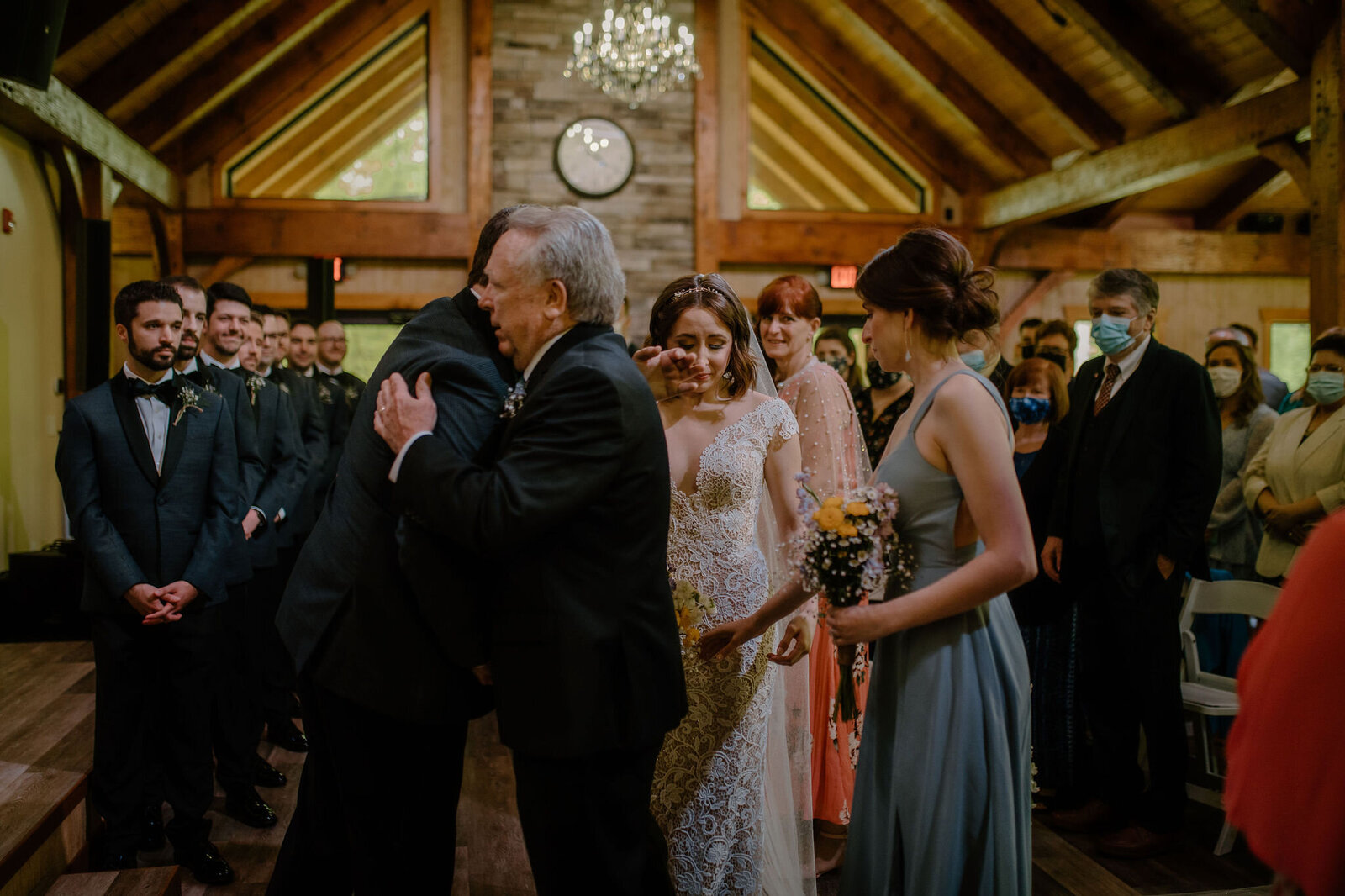 father hugging groom and emotional bride crying in background