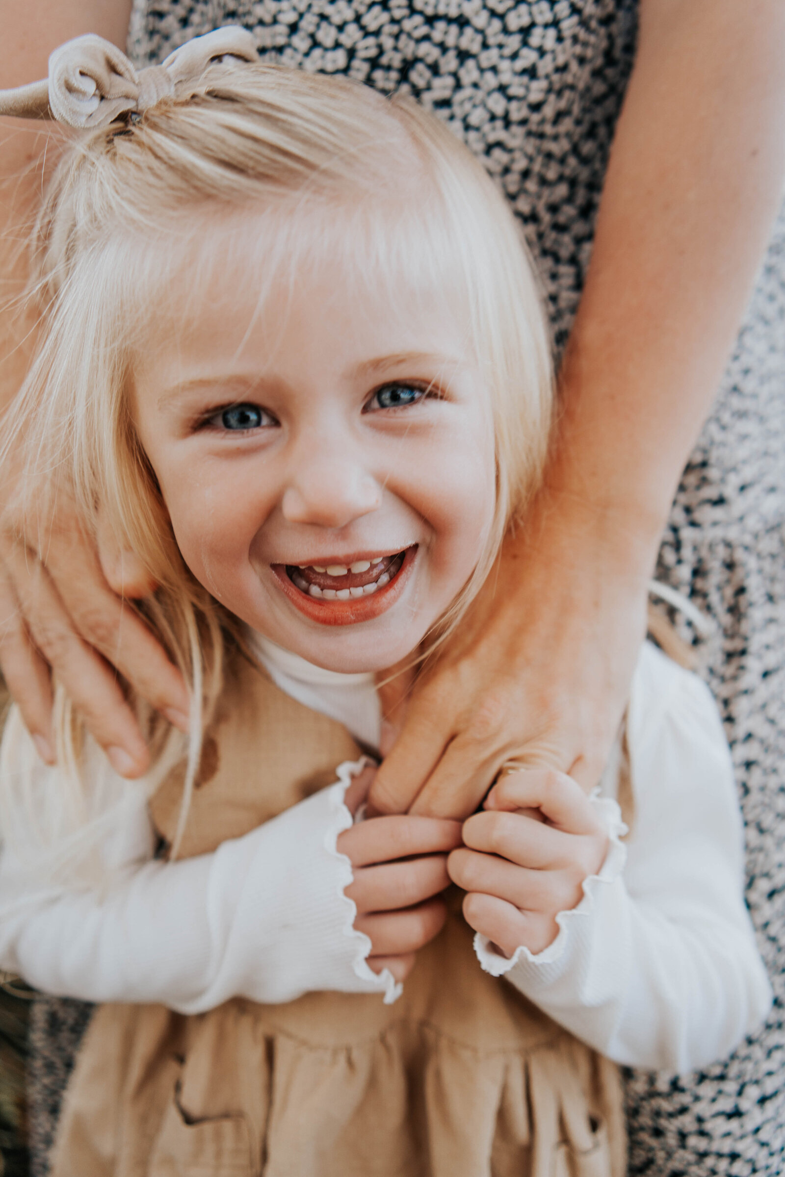 little girl smiling at the camera holding mother's hand captured by Idaho Falls photographer