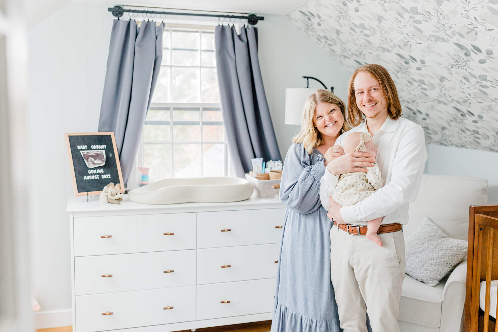 Mom and dad smiling in the nursery with a sleeping baby