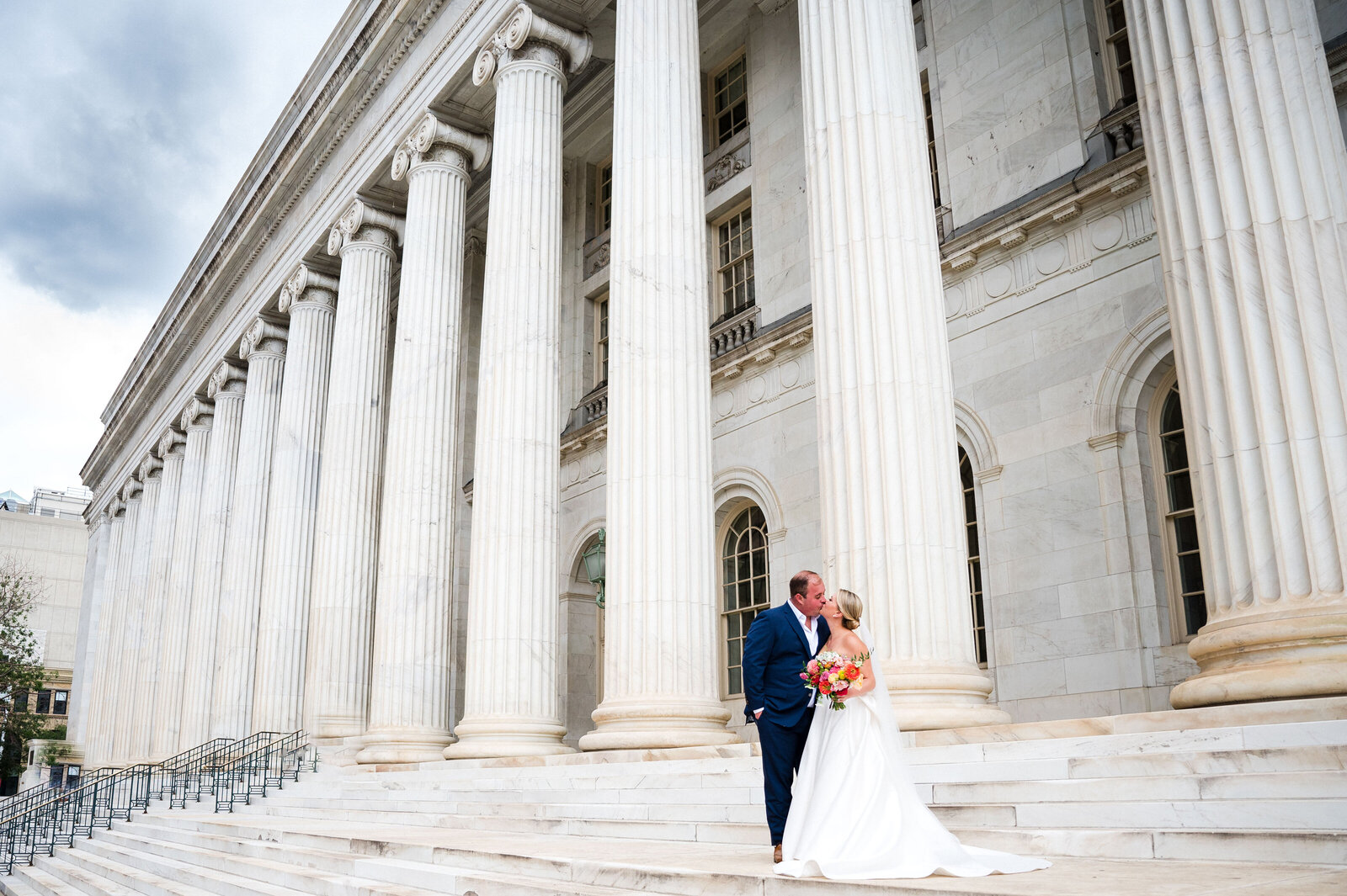 A bride and groom share a kiss on the front steps of a downtown Denver building.