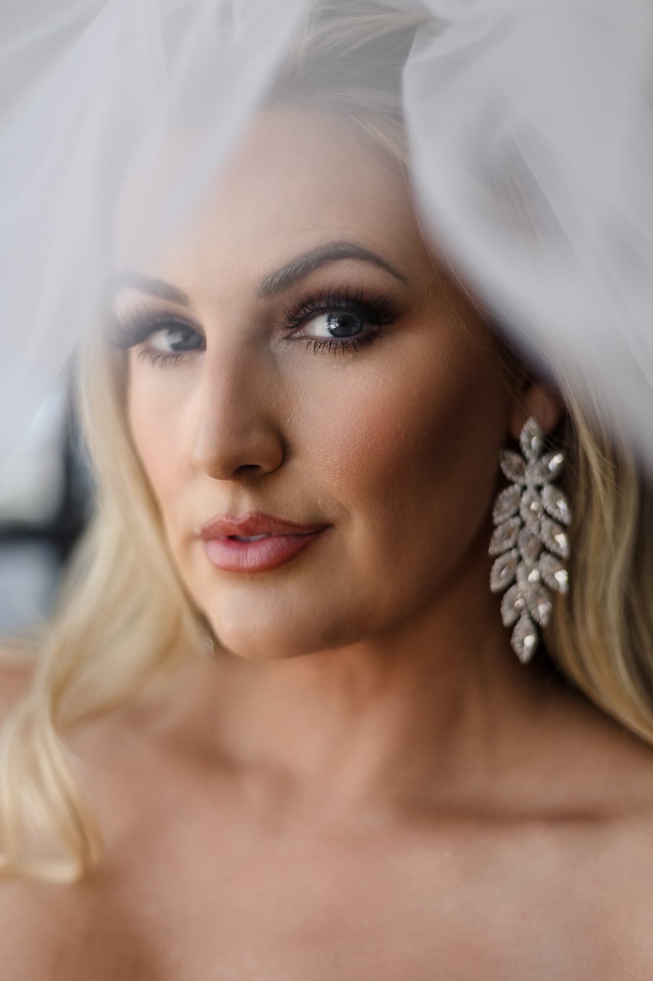 Luxury bridal portrait by Houston wedding photographer Logrono & Co., featuring a close-up of a bride with glamorous makeup, crystal earrings, and soft veil lighting.
