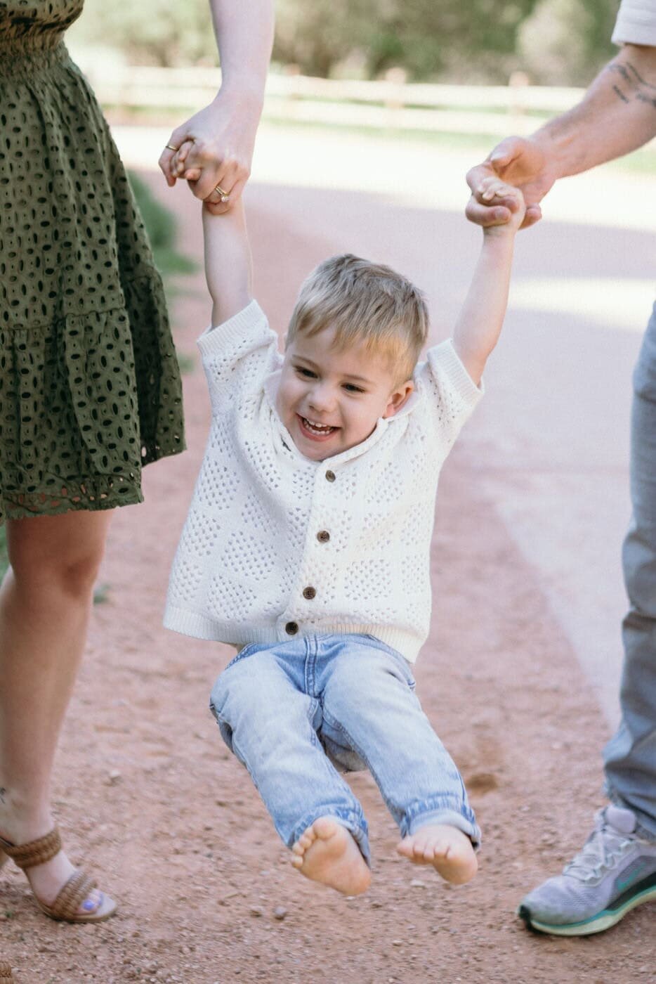 Two parents hold their toddler's hands and swing him between them.
