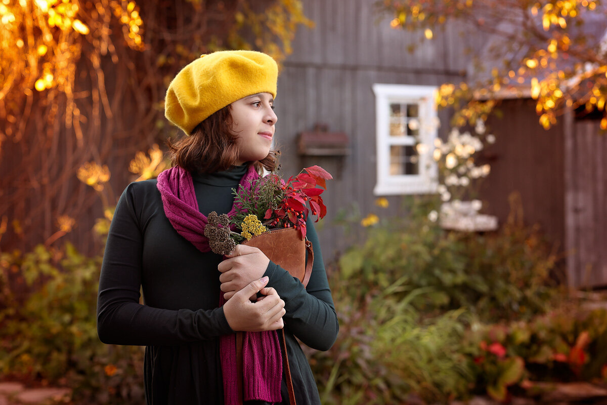Girl in yellow autumn biretta hat with fall flowers in Saint-Ambroise-de-Kilarne farm in Quebec.