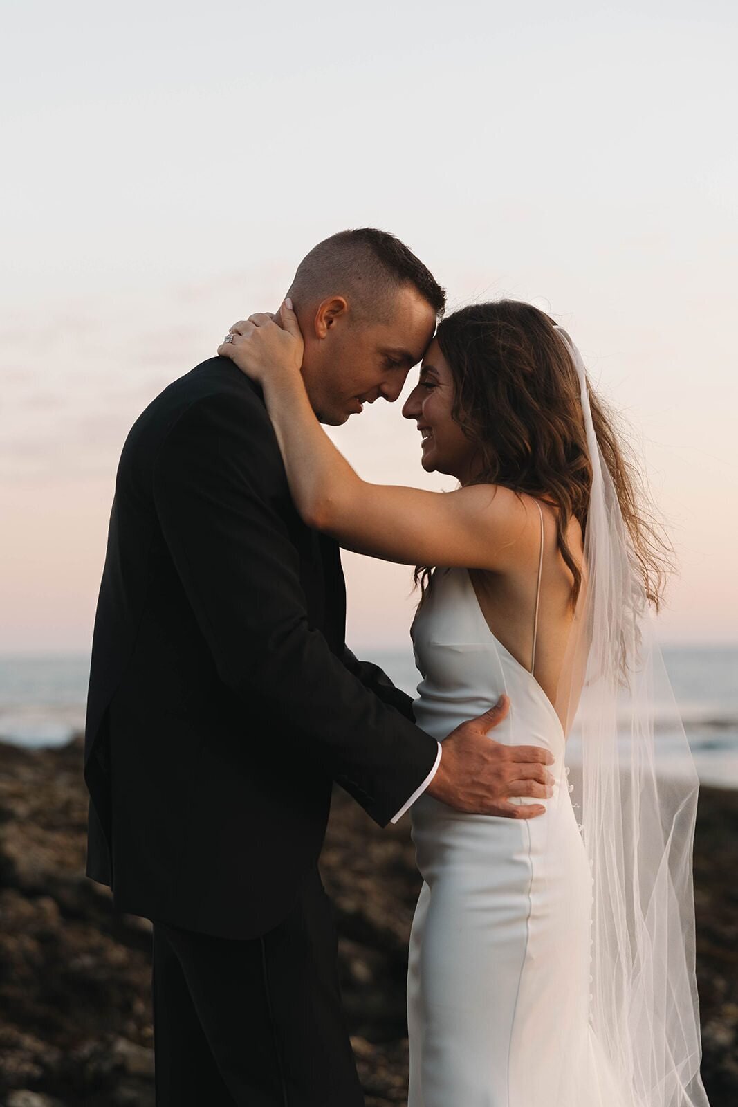 Bride and groom touching foreheads on the beach at sunset