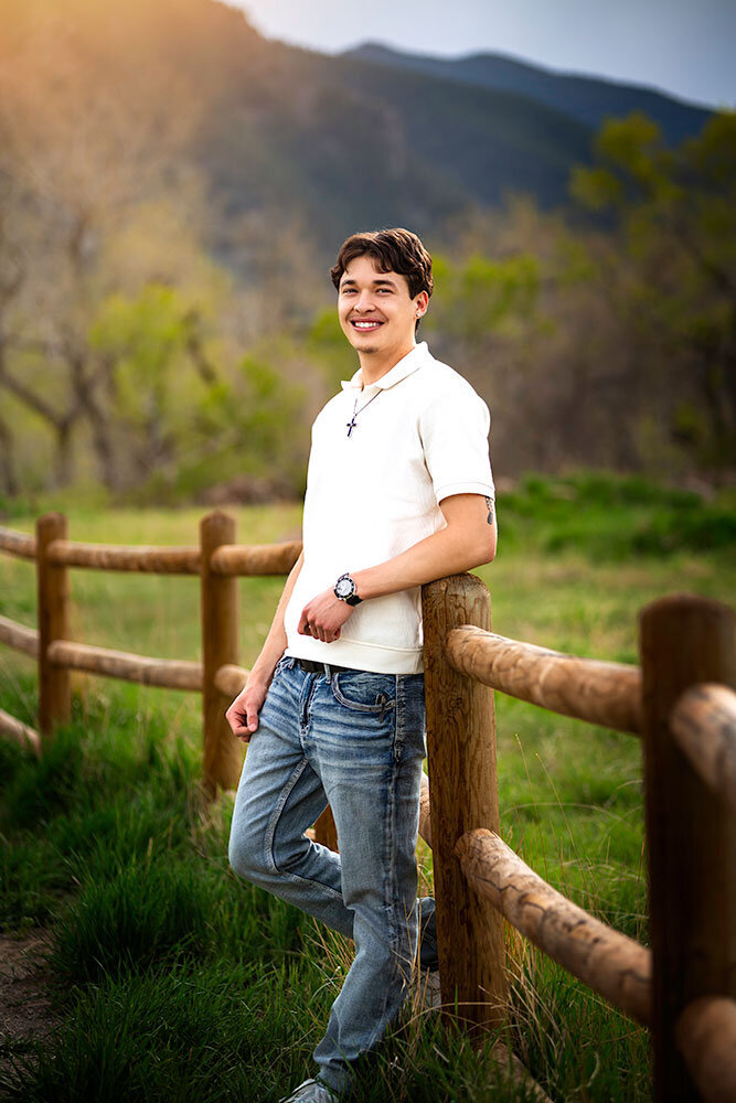 high-school-boy-senior-portrait-smiling-christian-cross-white-button-shirt-relaxed-leaning-against-fence-post-south-mesa-trailhead-boulder-yearbook
