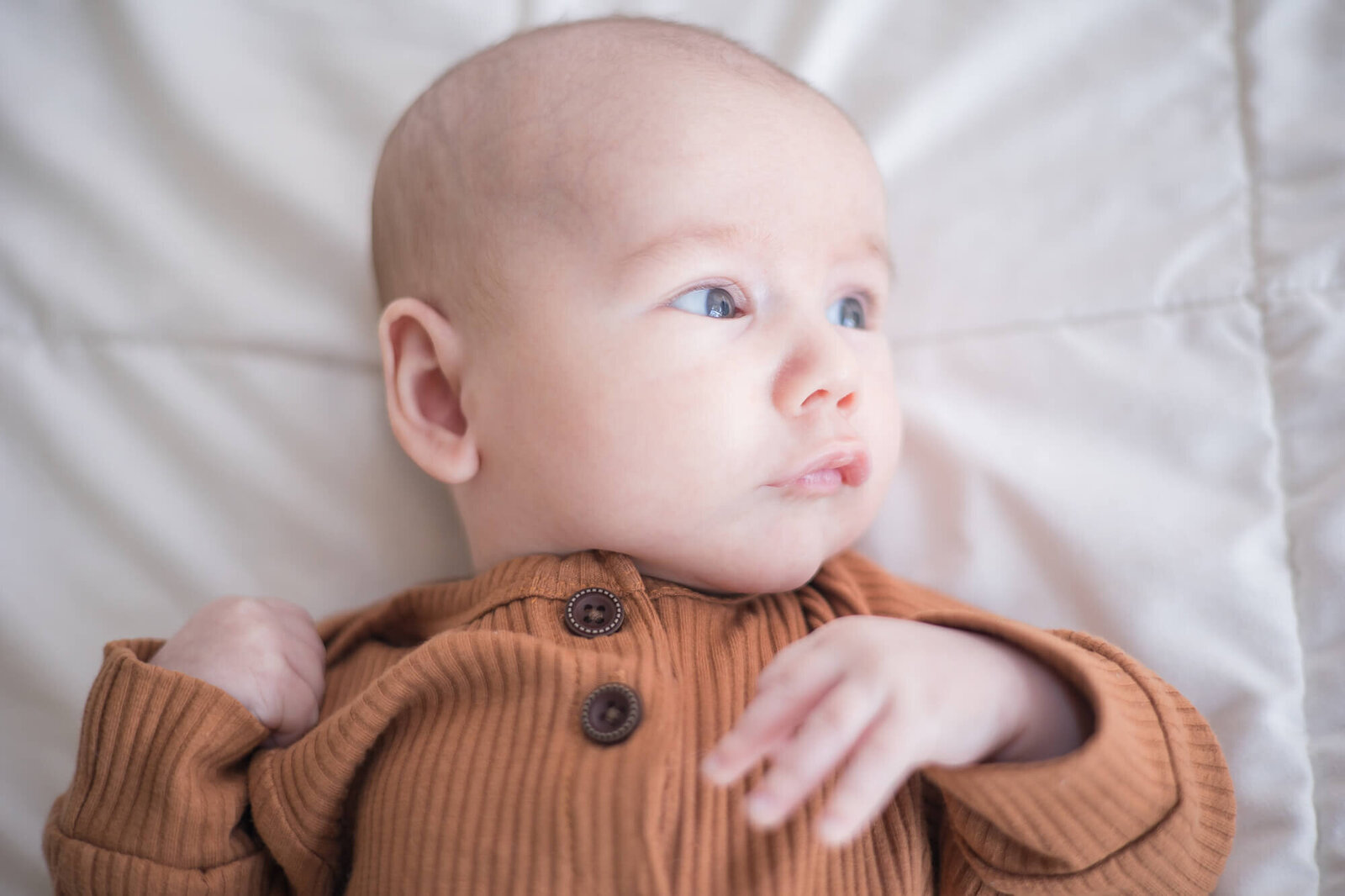 infant toddler boy lying on a bed, looking at window light