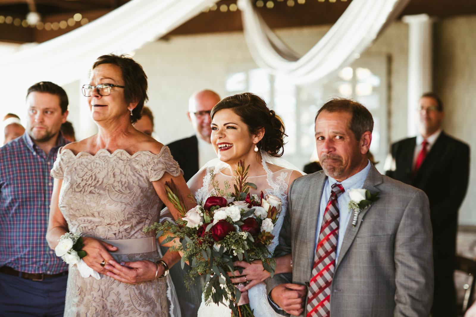 Bride walking down the aisle with her mother and father laughing and crying