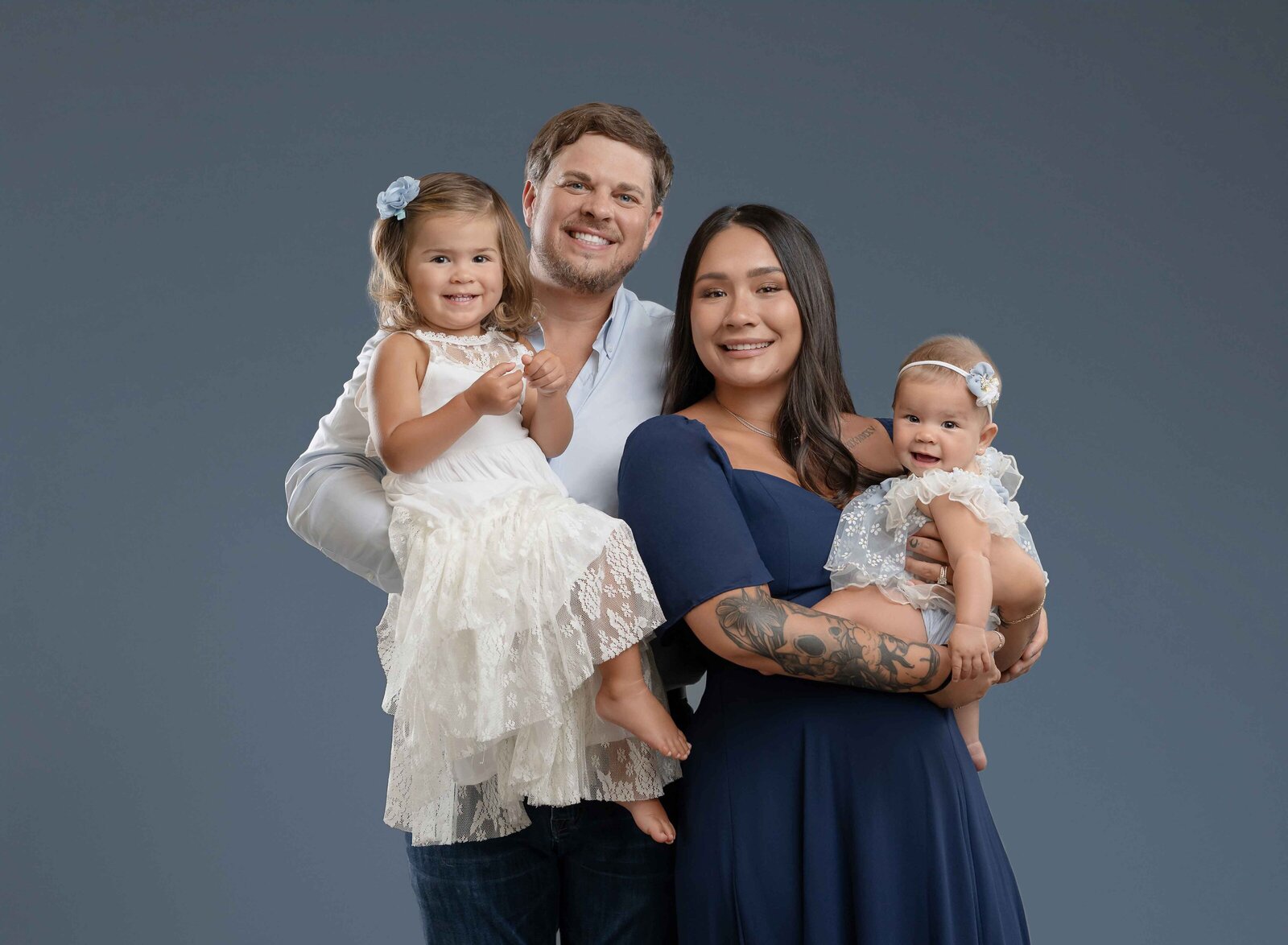 Family of 4 taking professional photo. Mom holding baby girl and Dad holding 2 year old big sister.