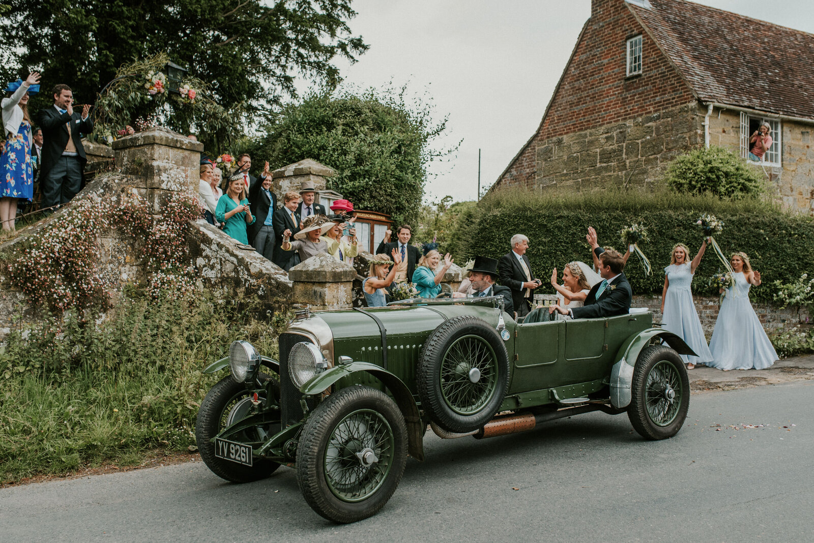 bride and groom wave at guests outside church from their vintage car