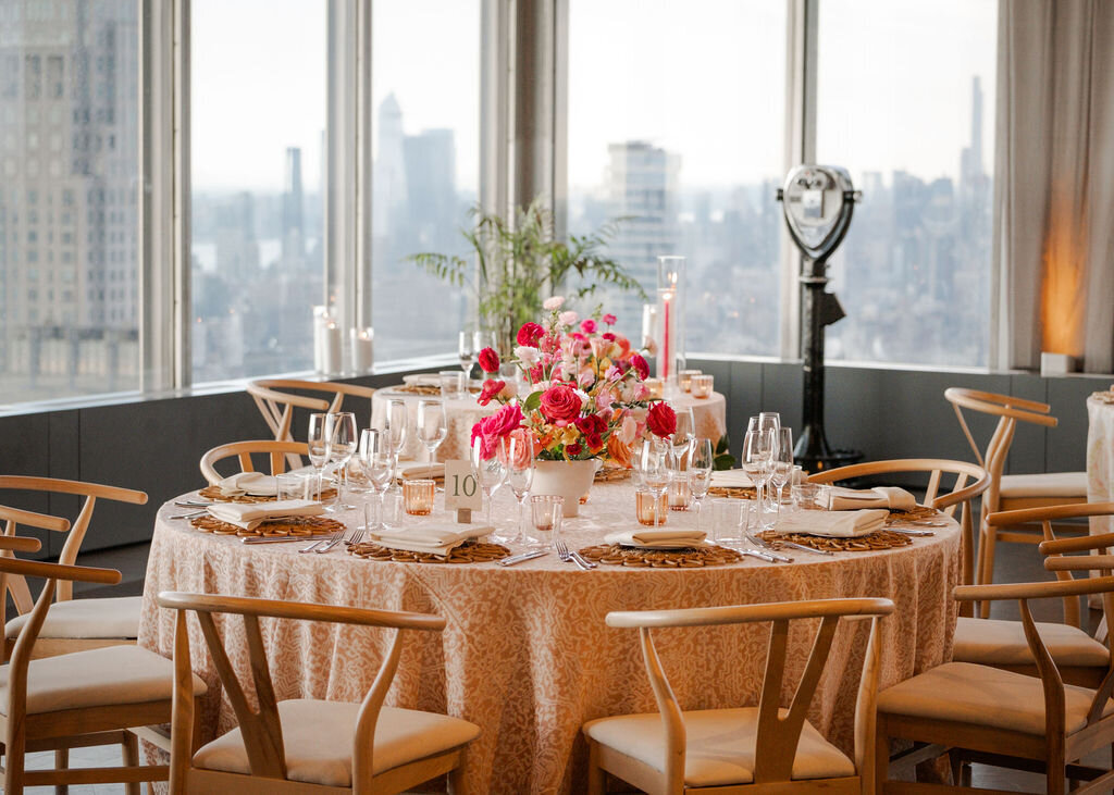 Sophisticated wedding reception setup on a rooftop venue with panoramic city skyline views, round tables, and floral centerpieces.