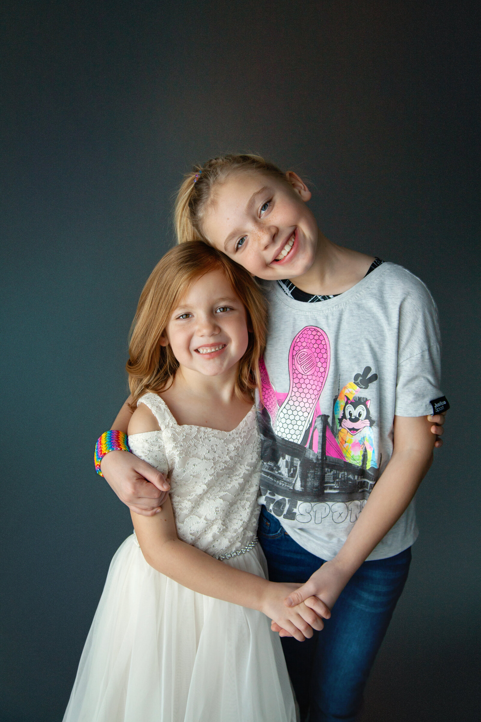 Sisters embracing and smiling with gray background.