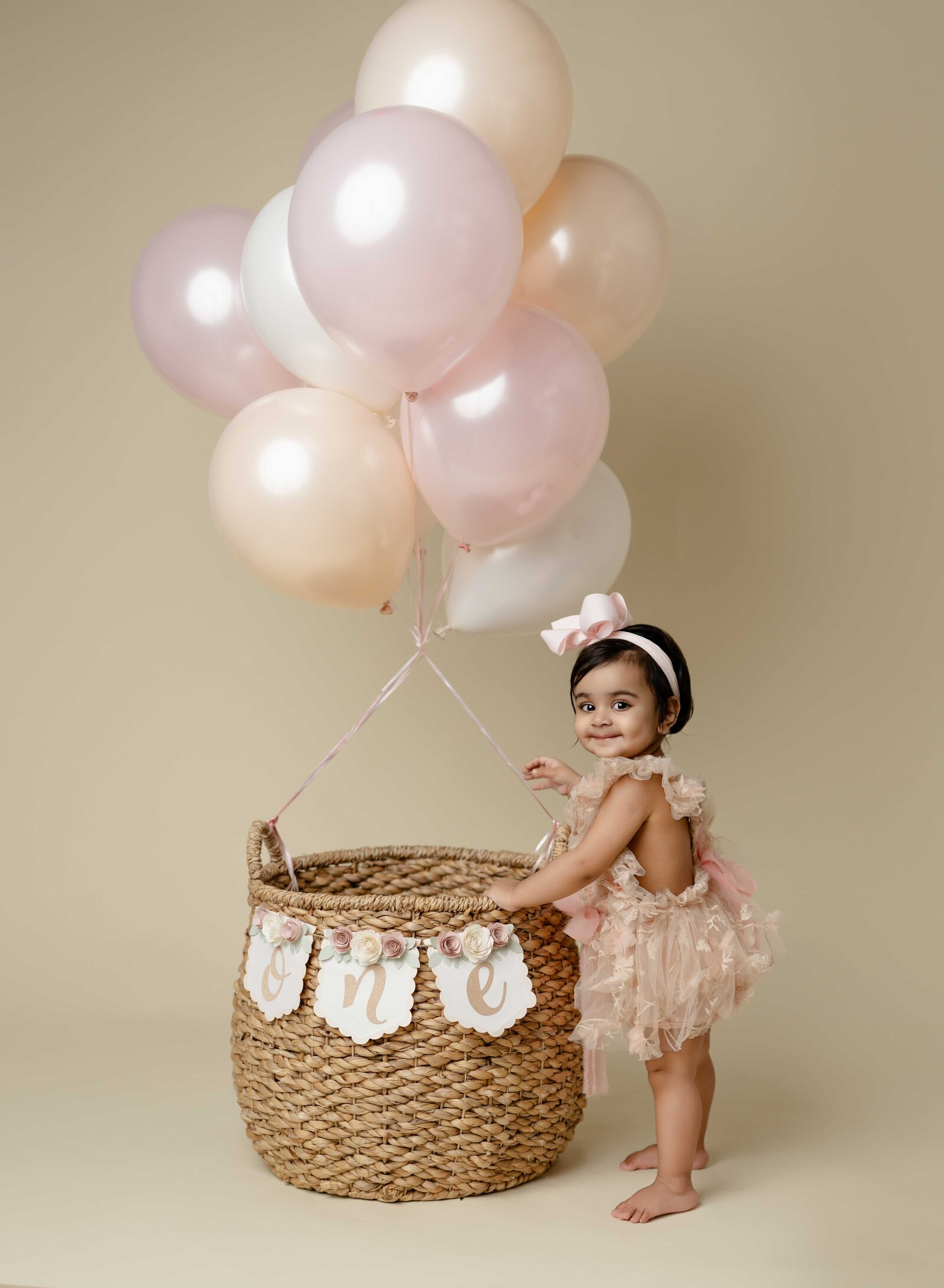 Baby girl standing by a balloon filled basket and smiling. 1st birthday photo taken by Jenni Nikki Photography in Atlanta, GA.