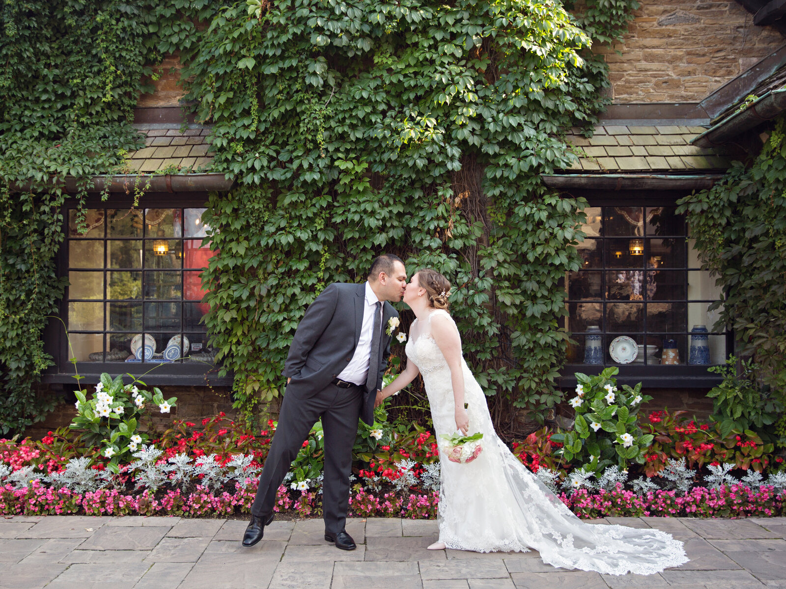 bride and groom kissing in front of ivy wall with flowers