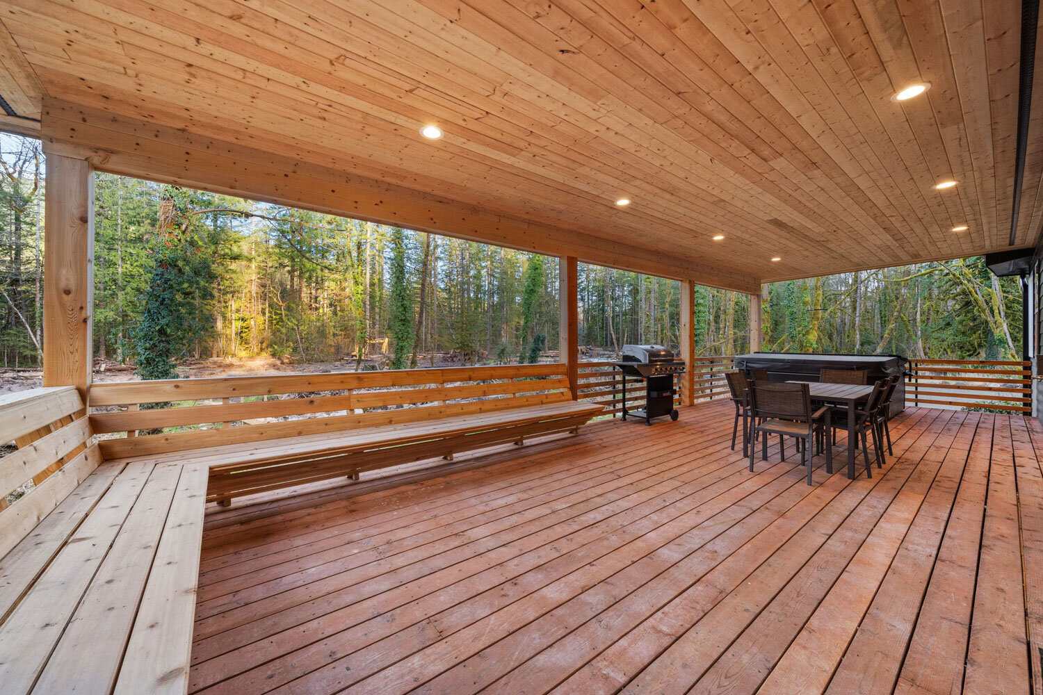 Large wooden deck with a bench and dining table surrounded by trees