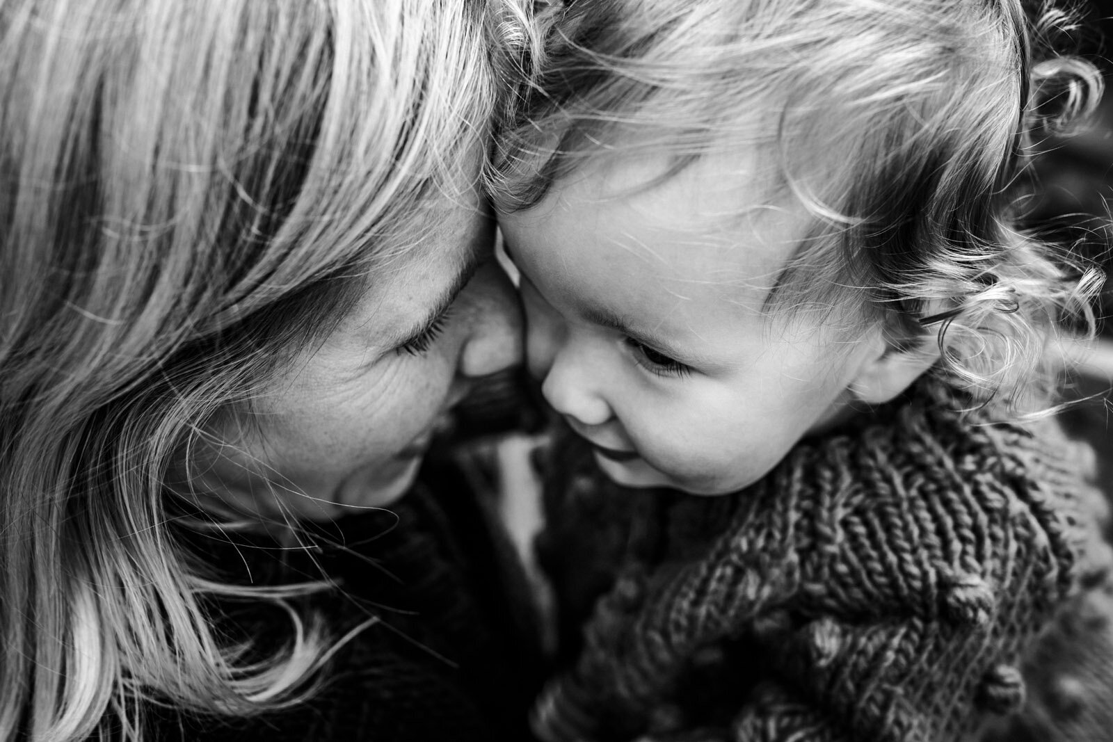 close up of mom and toddler daughter snuggling up close to each other and smiling
