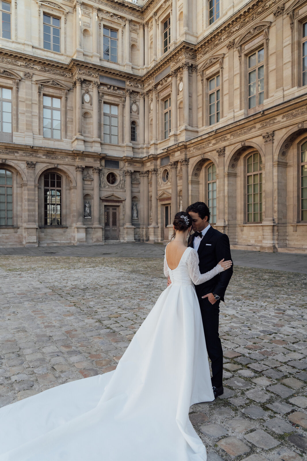 Luxe trouwjurk met vierkante halslijn kanten top lange mouwen en satijnen rok met plooien en een grote sleep met knoopjes op de rug gefotografeerd in Parijs

