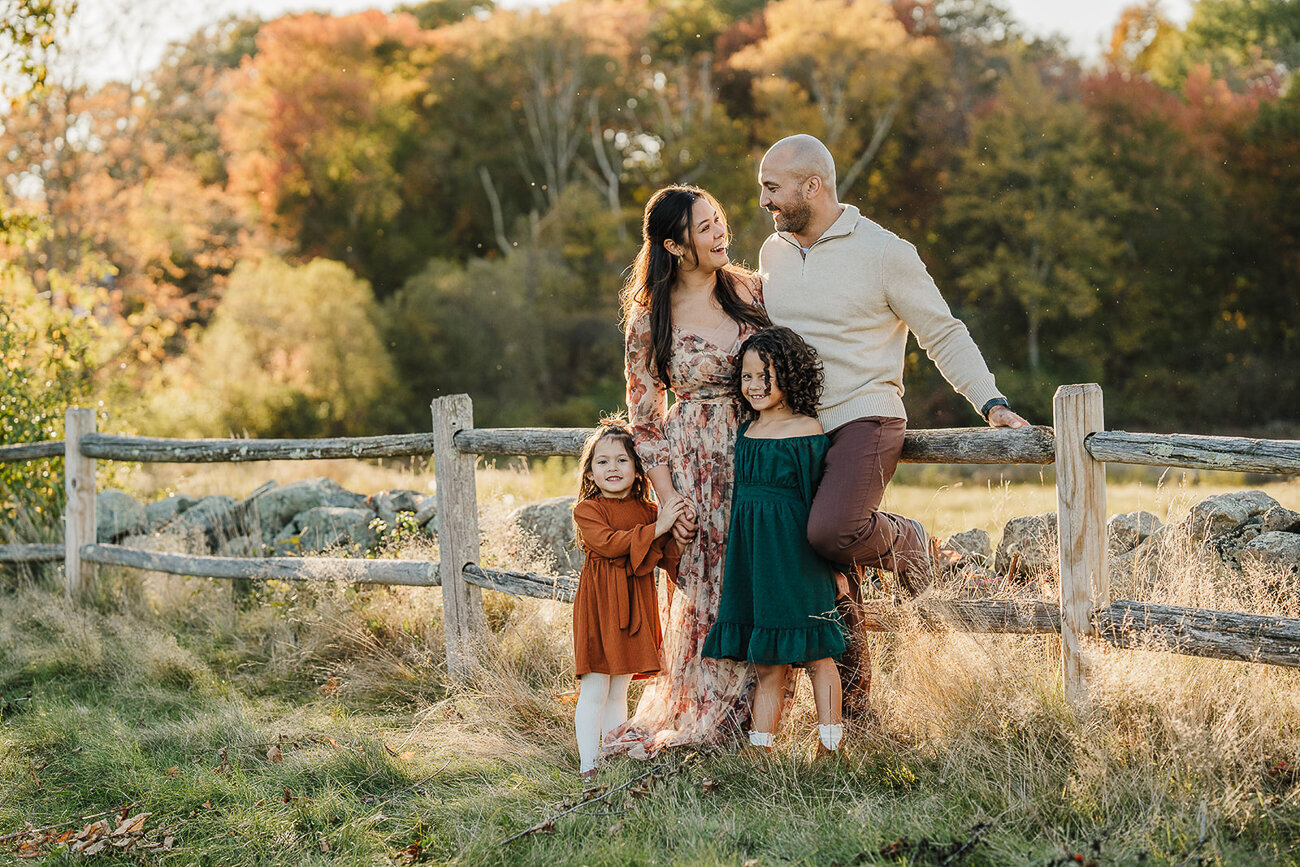 family of four lean against wooden fence in autumn in boston