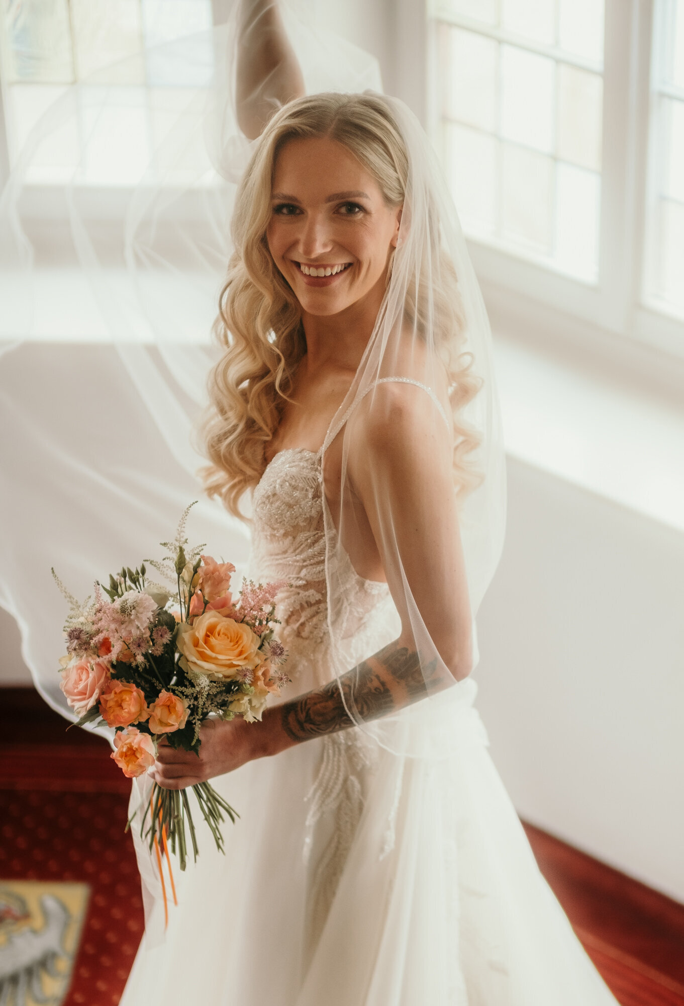 A bride holds up her bouquet with one hand and her veil with the other. Wedding Photographer Karin Busch Los Angeles.
