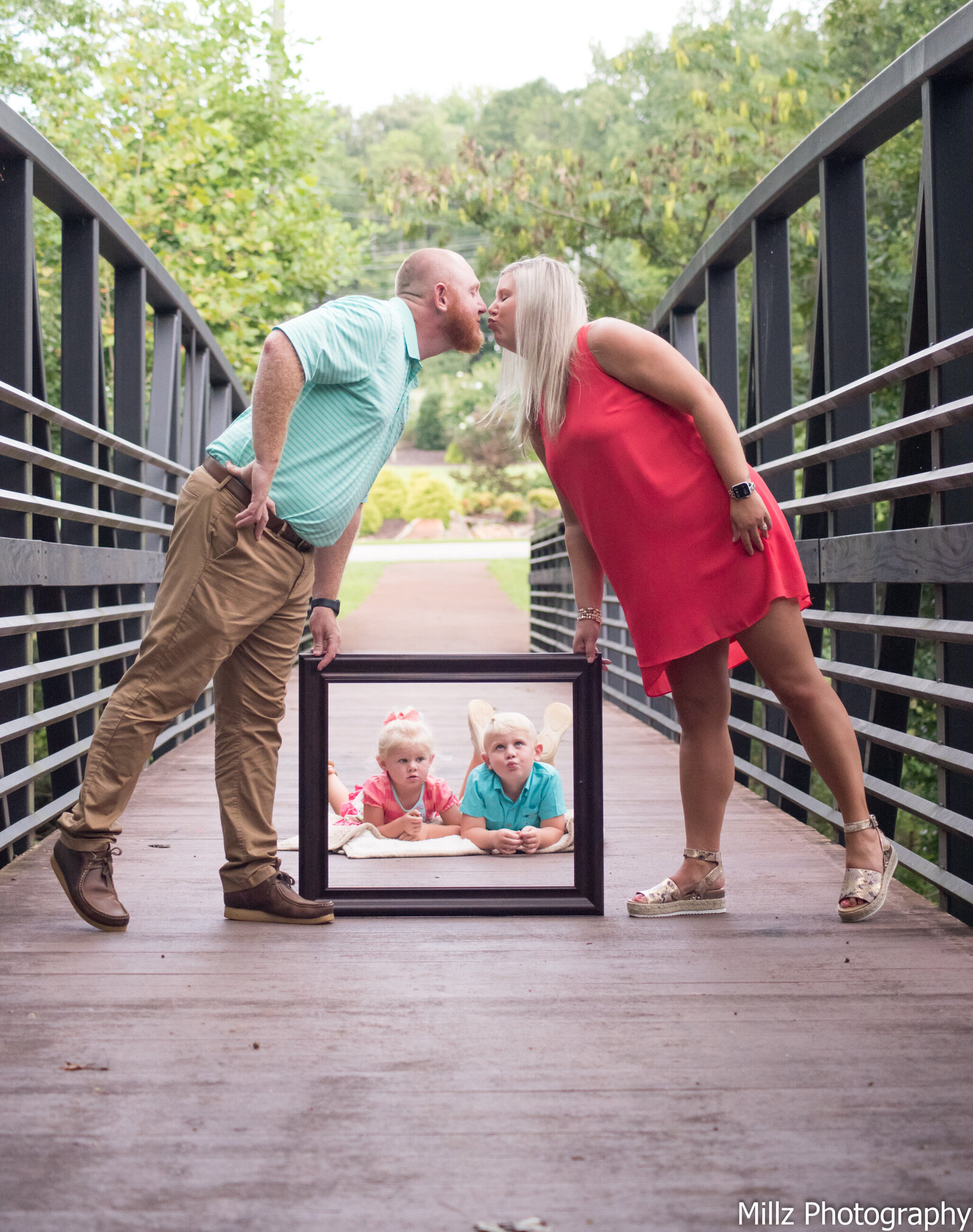 mom and dad sharing a kiss while holding a picture frame over their son and daughter photographed by Millz Photography in Greenville, SC