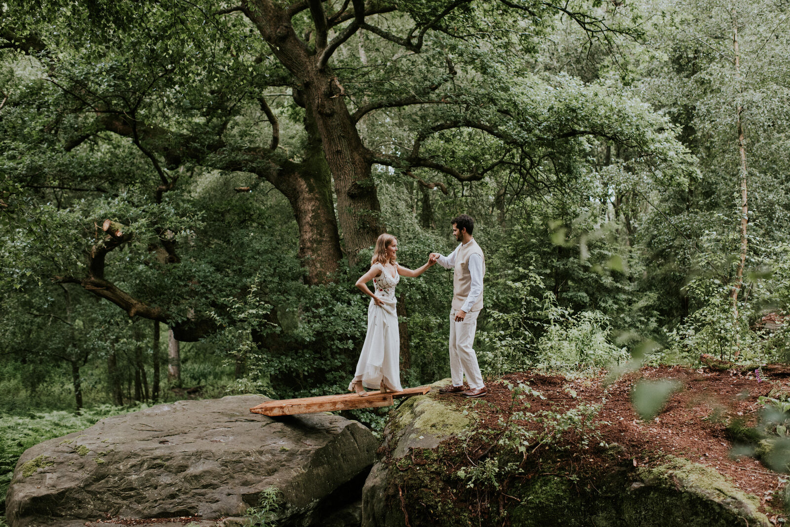 Groom helping bride over a bridge at their woodland wedding