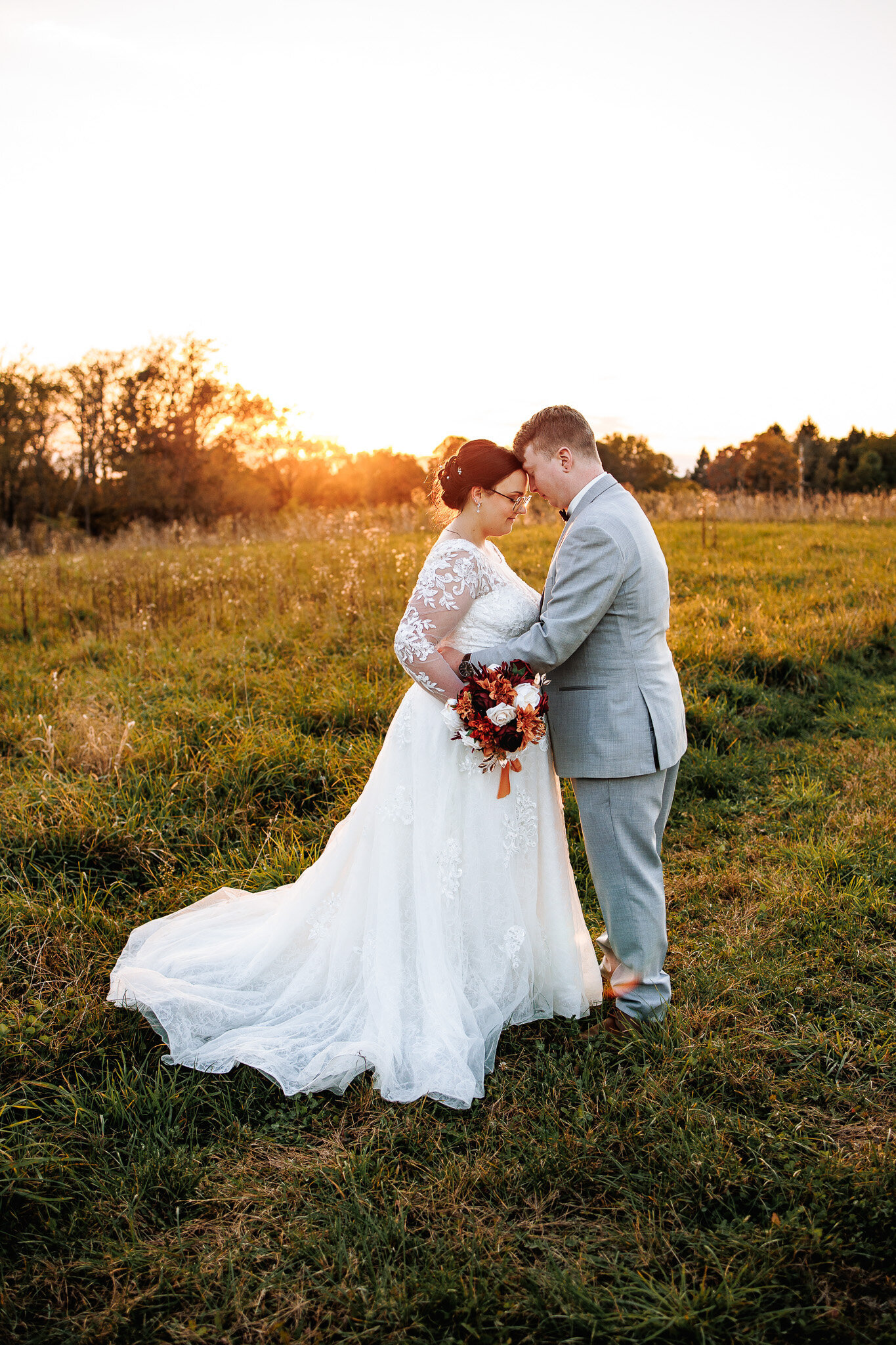 Foreheads touching, a bride and groom stand close together for a photo with a golden sunset in the background 